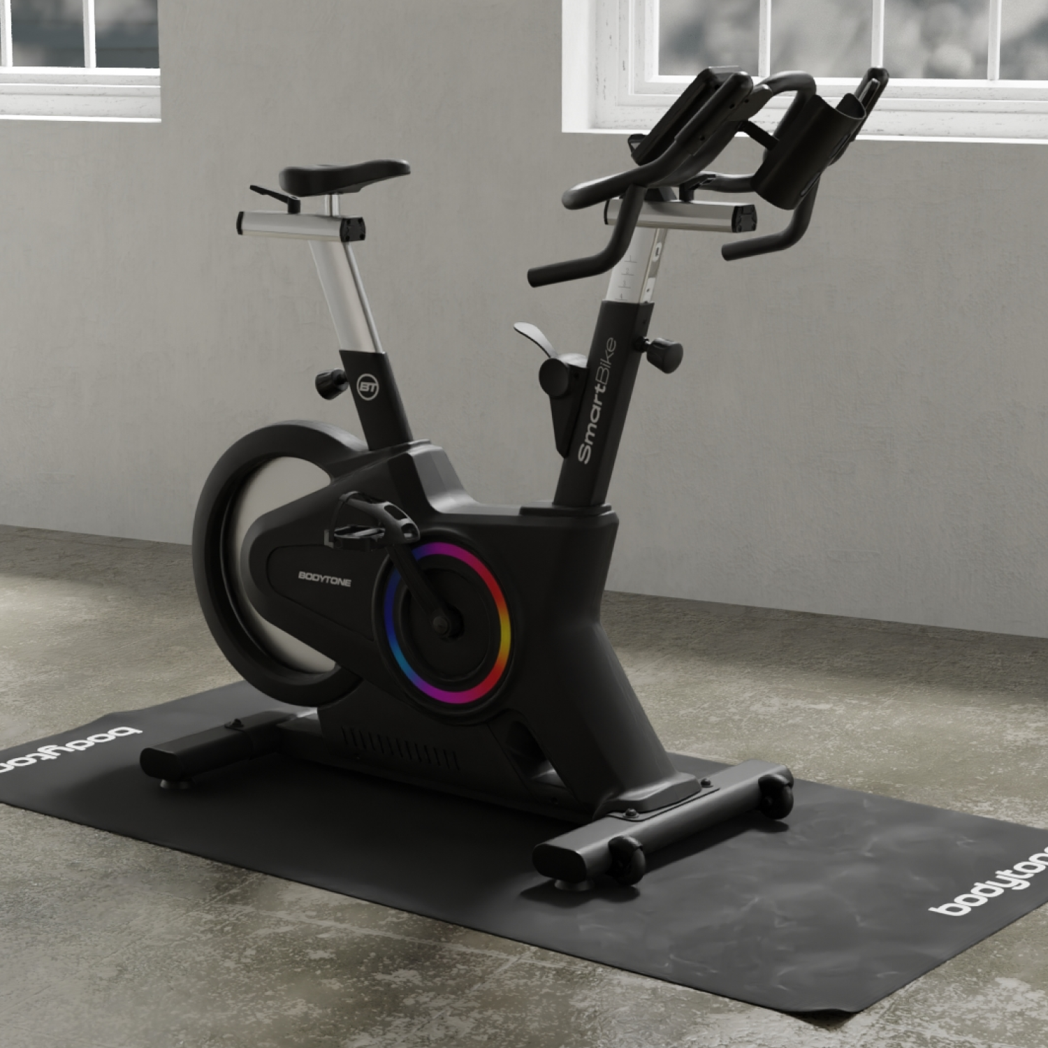 Bici da spinning nera su un tappetino nero, vicino a una finestra. La bici ha un display colorato.