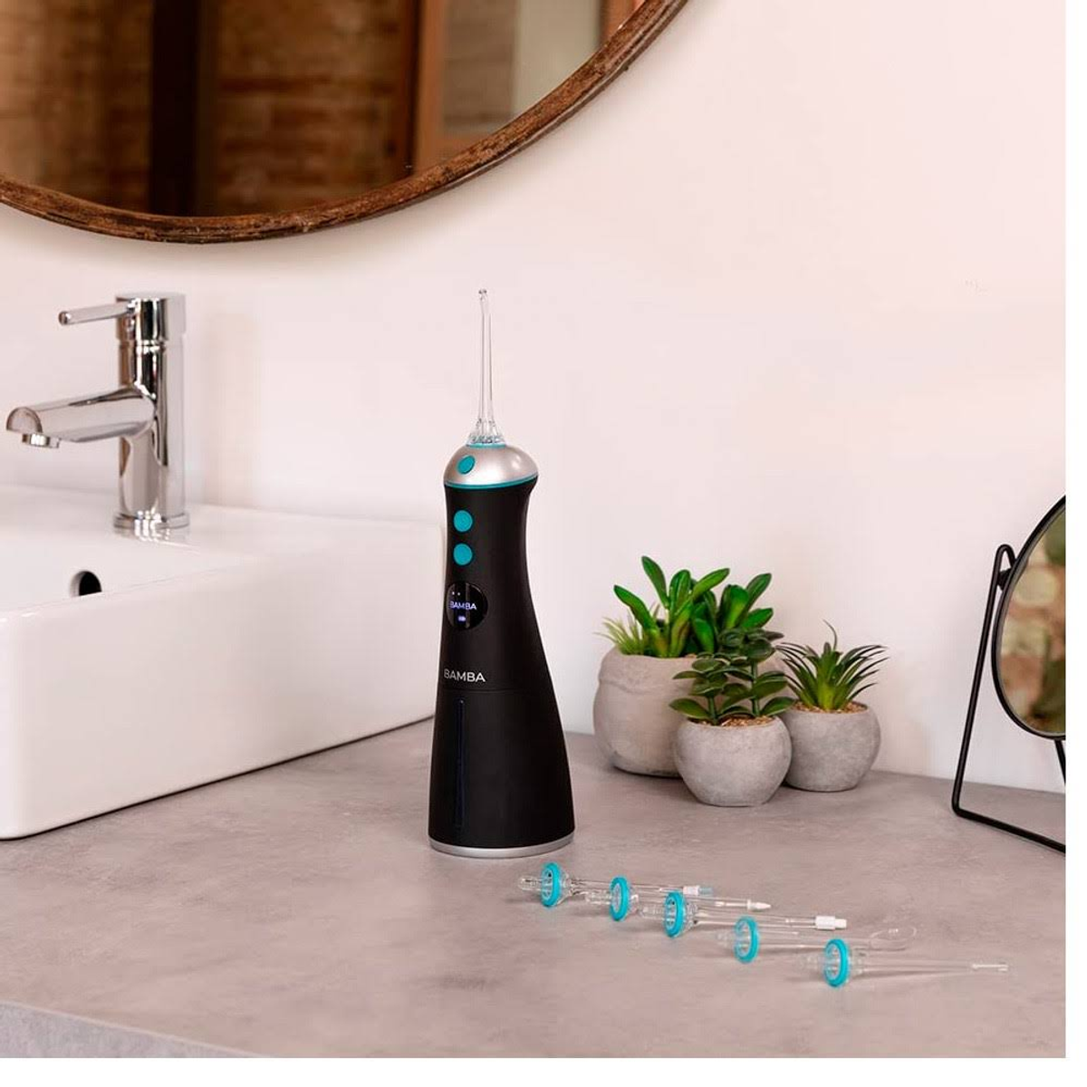 Czarny i srebrny irygator do jamy ustnej z kilkoma końcówkami na blacie, w pobliżu małych roślin doniczkowych i lustra.