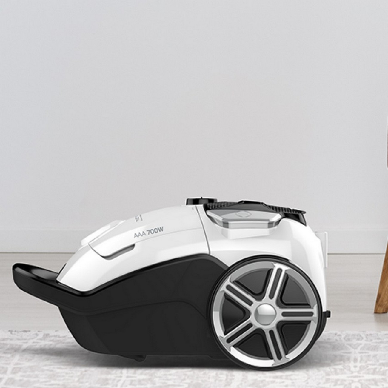 Biały i czarny odkurzacz stoi na wzorzystym dywanie na tle białej ściany.