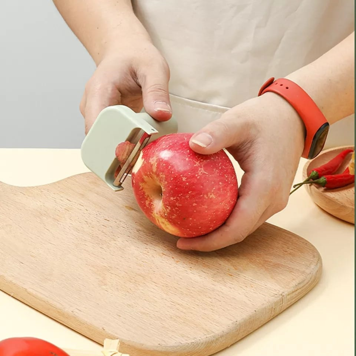 Persona pelando una manzana roja con un pelador en una tabla de madera.