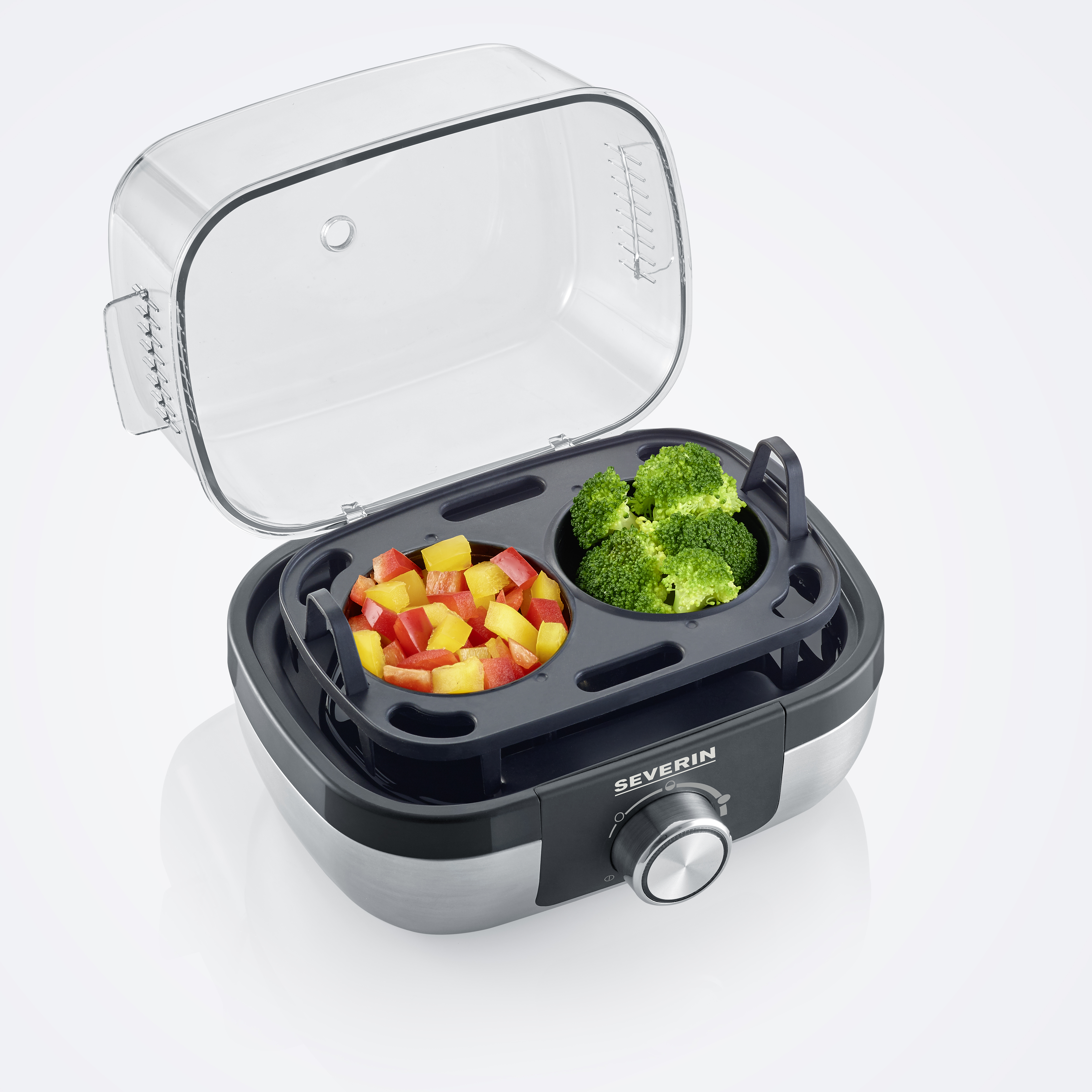 Parowar Severin z dwoma przegrodami zawierającymi brokuły i paprykę. Znajduje się na białej powierzchni.