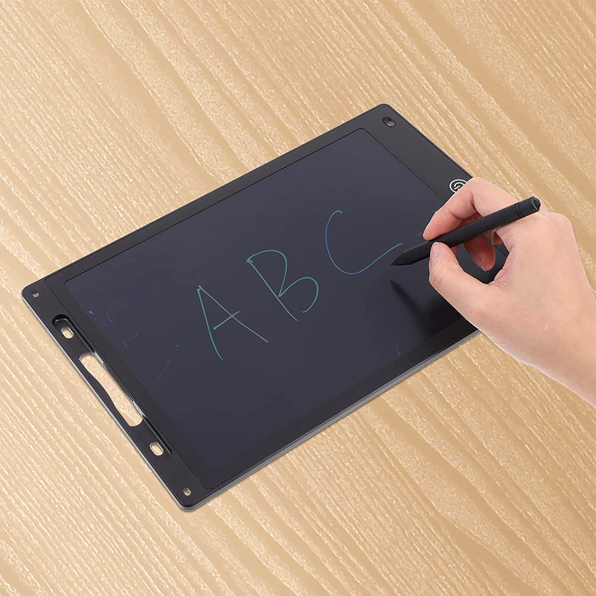 Una mano que escribe 'ABC' en una tableta negra con un lápiz. La tableta está sobre una superficie de madera.