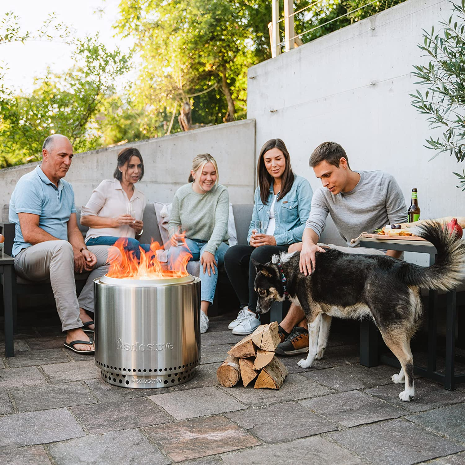 Gruppe von Leuten, Hund und Feuerstelle auf einer Terrasse.