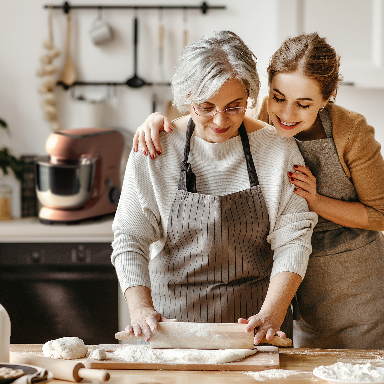 Due donne, una più anziana, che cucinano insieme, con farina e un mixer sullo sfondo.