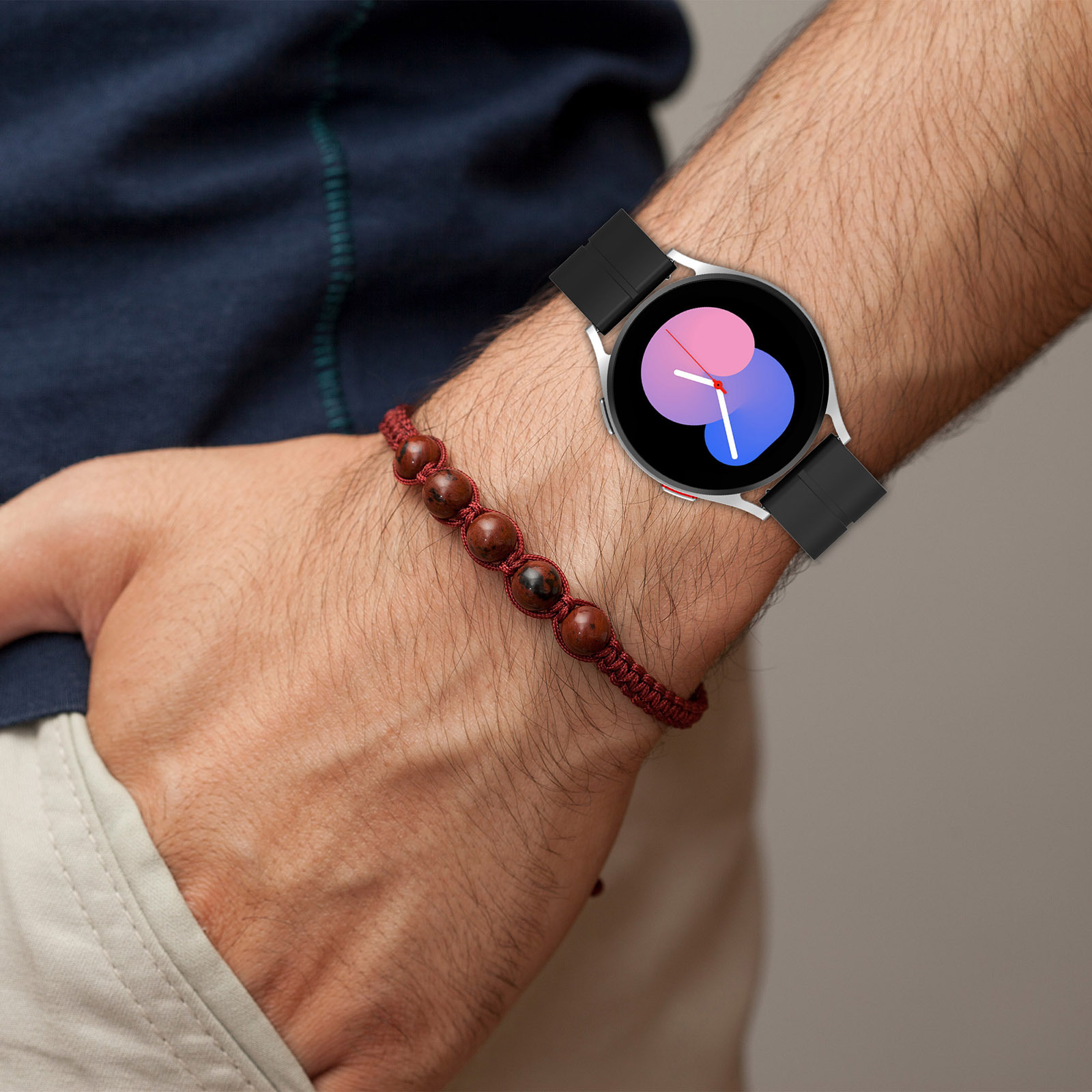 Nahaufnahme eines Handgelenks mit Smartwatch und Perlenarmband. Die Uhr hat ein schwarzes Band.