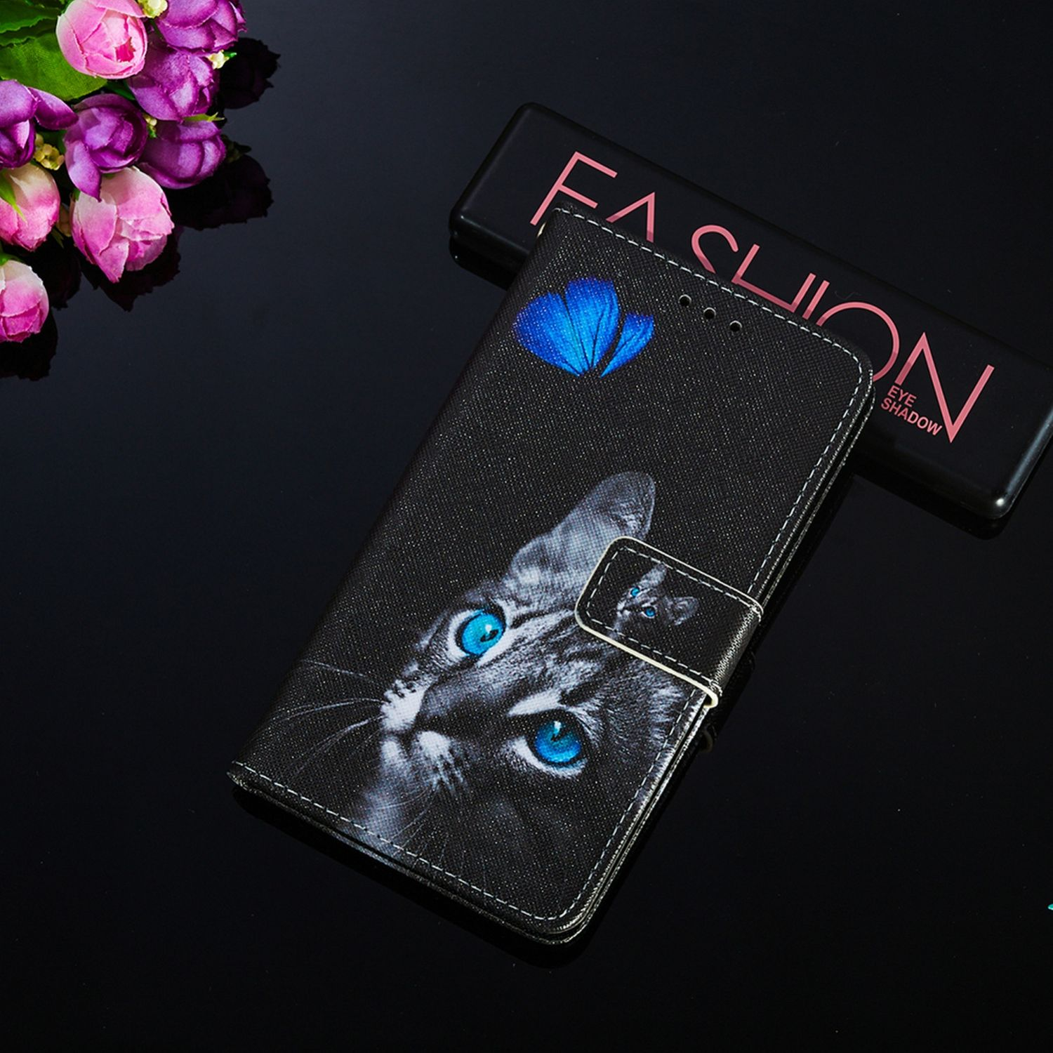 Eine schwarze Handyhülle mit Katzenmotiv, Schmetterling und dem Wort Fashion. Schwarzer Hintergrund.