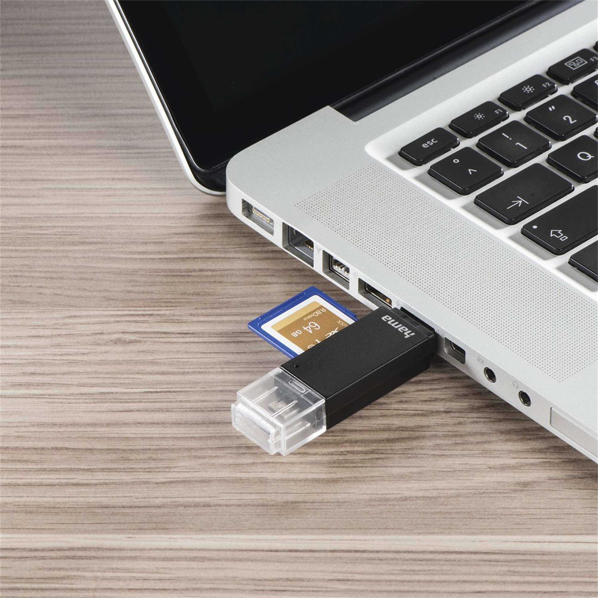 Laptop z włożoną pamięcią USB i kartą SD, na drewnianej powierzchni. Czarno-biały design.