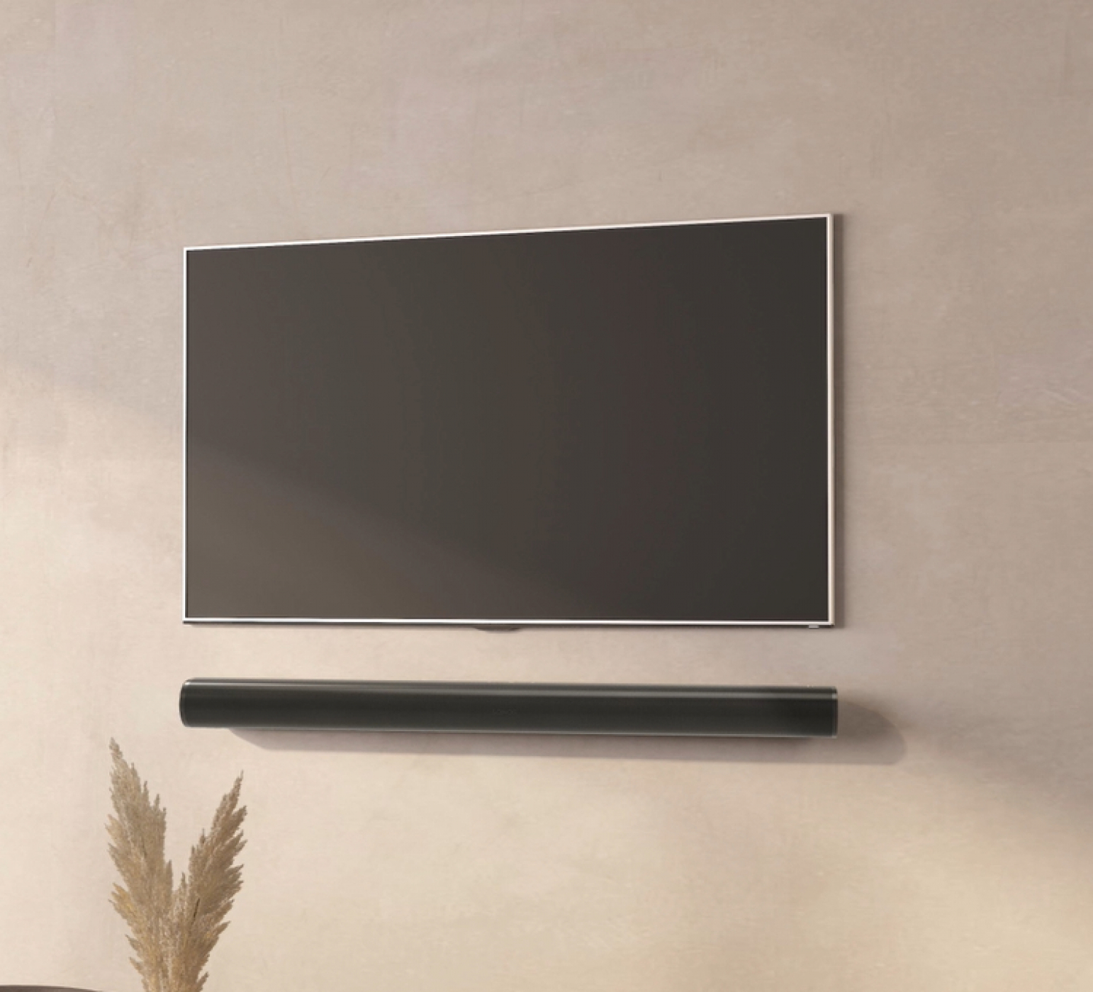 A large black TV is mounted on a wall above a soundbar. Dried plants are on the left.