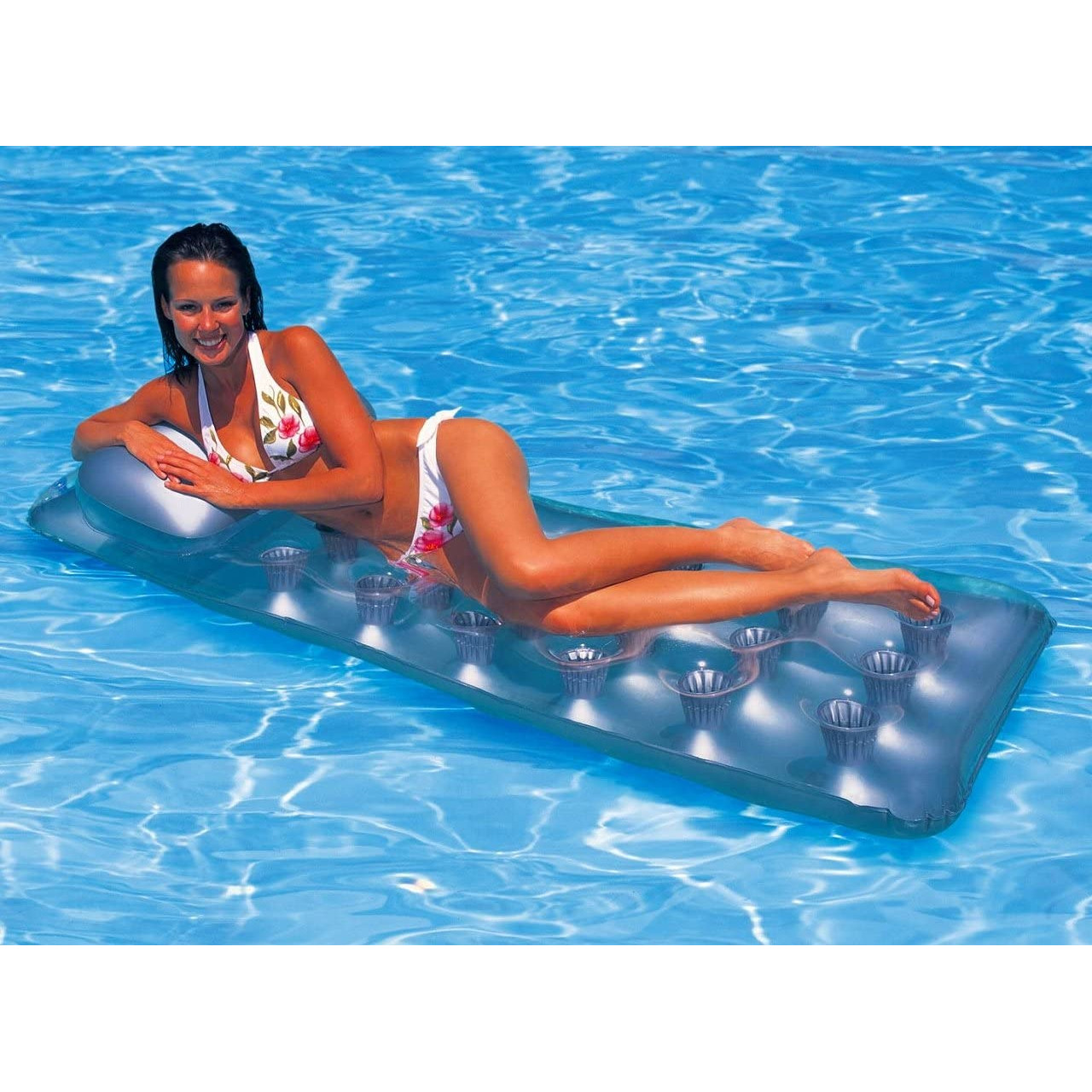 Kobieta w bikini na pływającym materacu w niebieskim basenie.