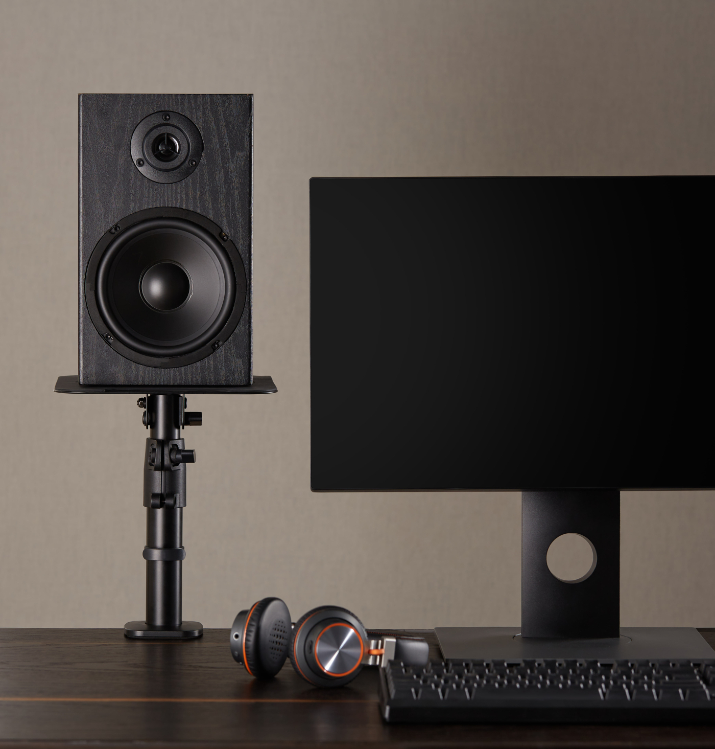 A speaker on a stand, headphones, and a monitor on a dark wooden desk.