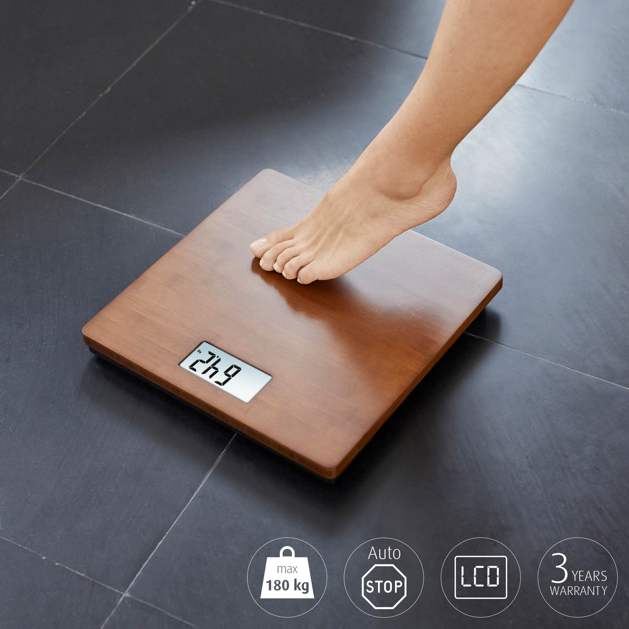 Pie de una persona en una báscula de madera con pantalla digital de 24.9, en suelo oscuro embaldosado.