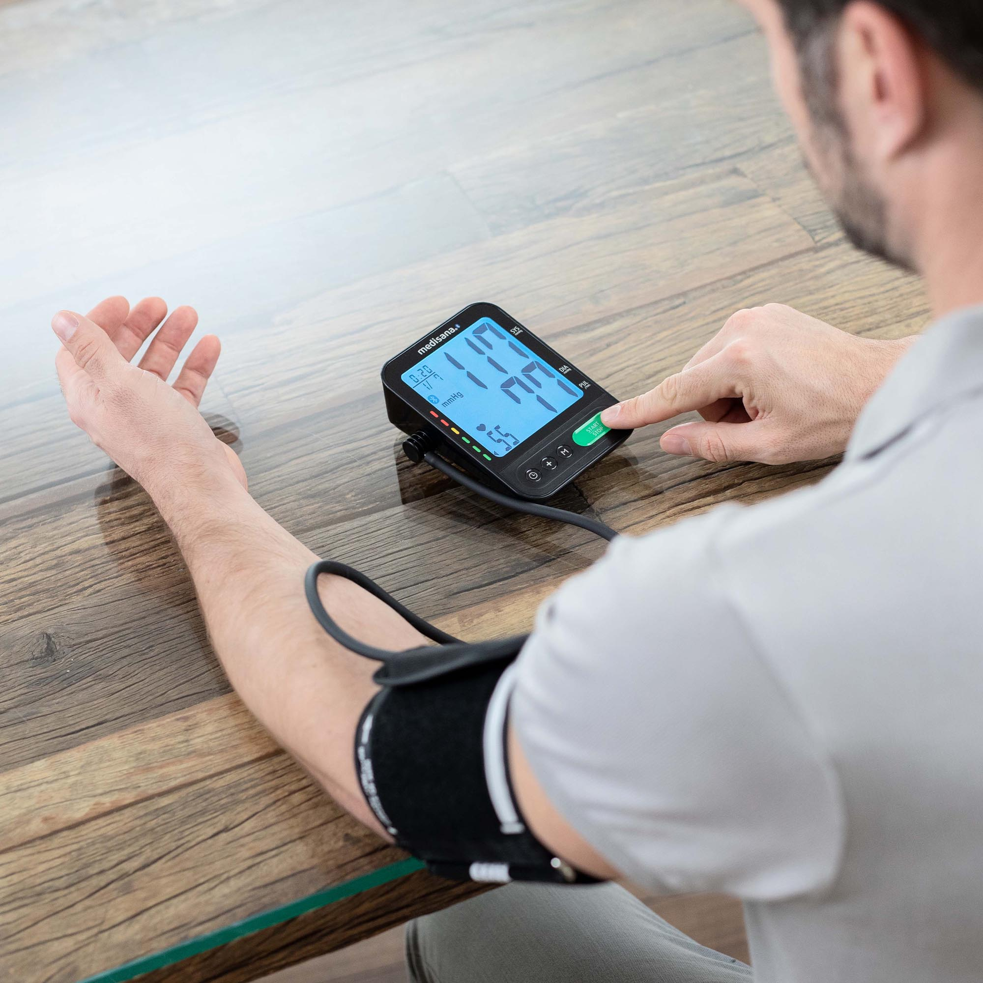 Un hombre usando un monitor de presión arterial en su brazo, sobre una mesa de madera.