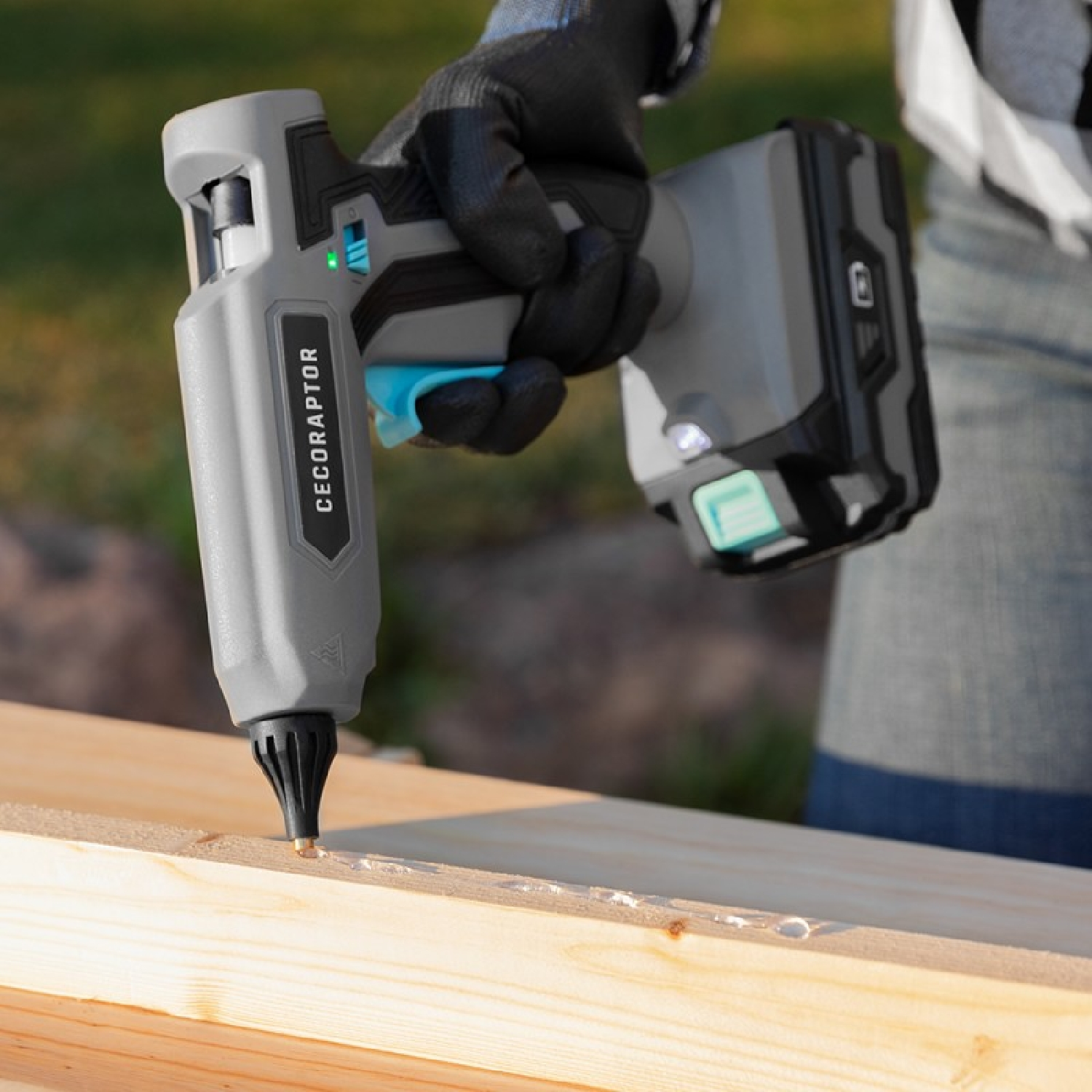 Szary pistolet do klejenia Cecoraptor nakładający klej na drewnianą powierzchnię.