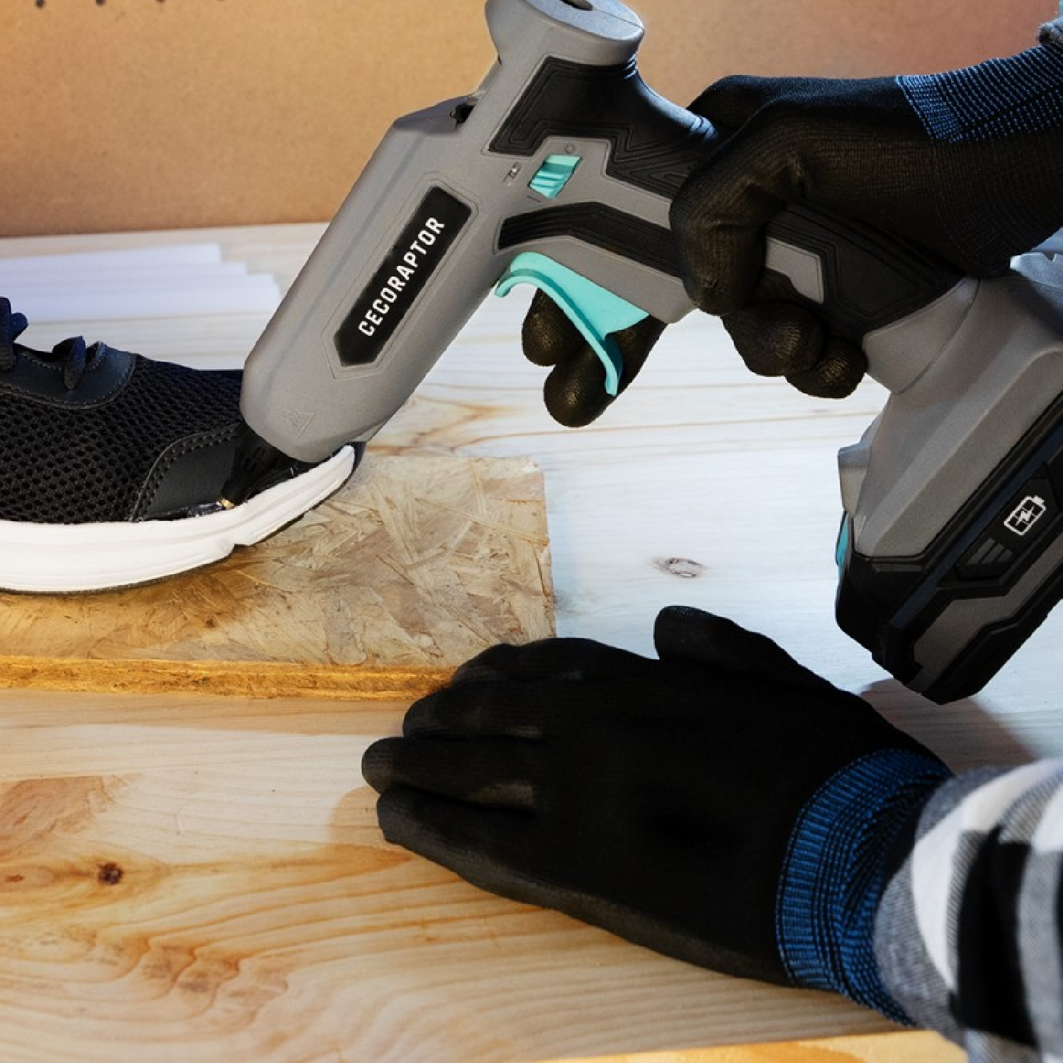 Ręce w rękawicach używające pistoletu do klejenia na bucie. But jest czarno-biały. Tło jest drewniane.