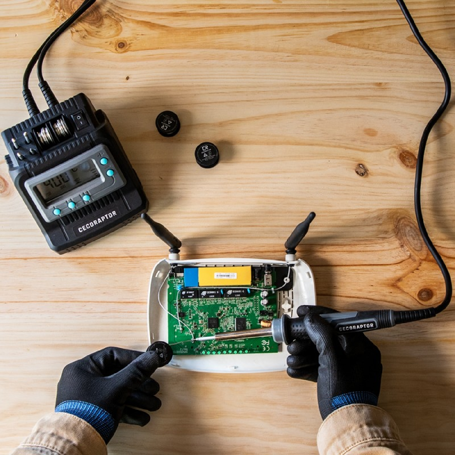 Ręce pracujące na płytce drukowanej z narzędziami, obok czarnego urządzenia z wyświetlaczem cyfrowym.