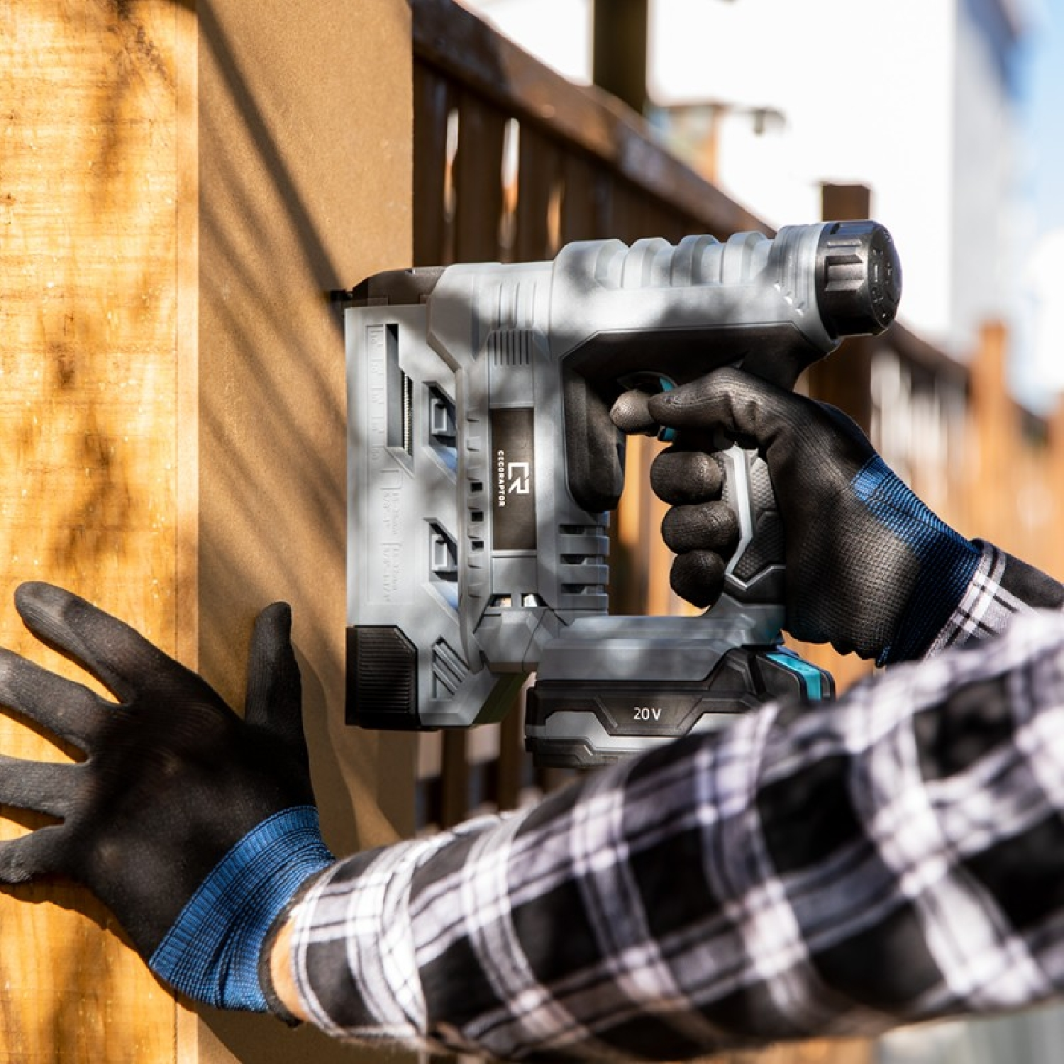 Person using a gray power nailer on a wooden fence.