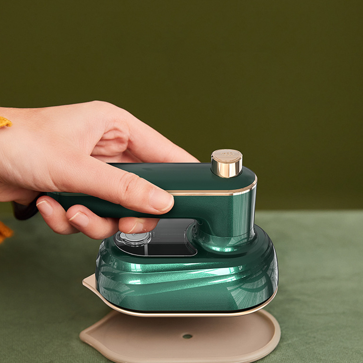 Una mano sosteniendo una mini plancha verde sobre una base de planchado beige.