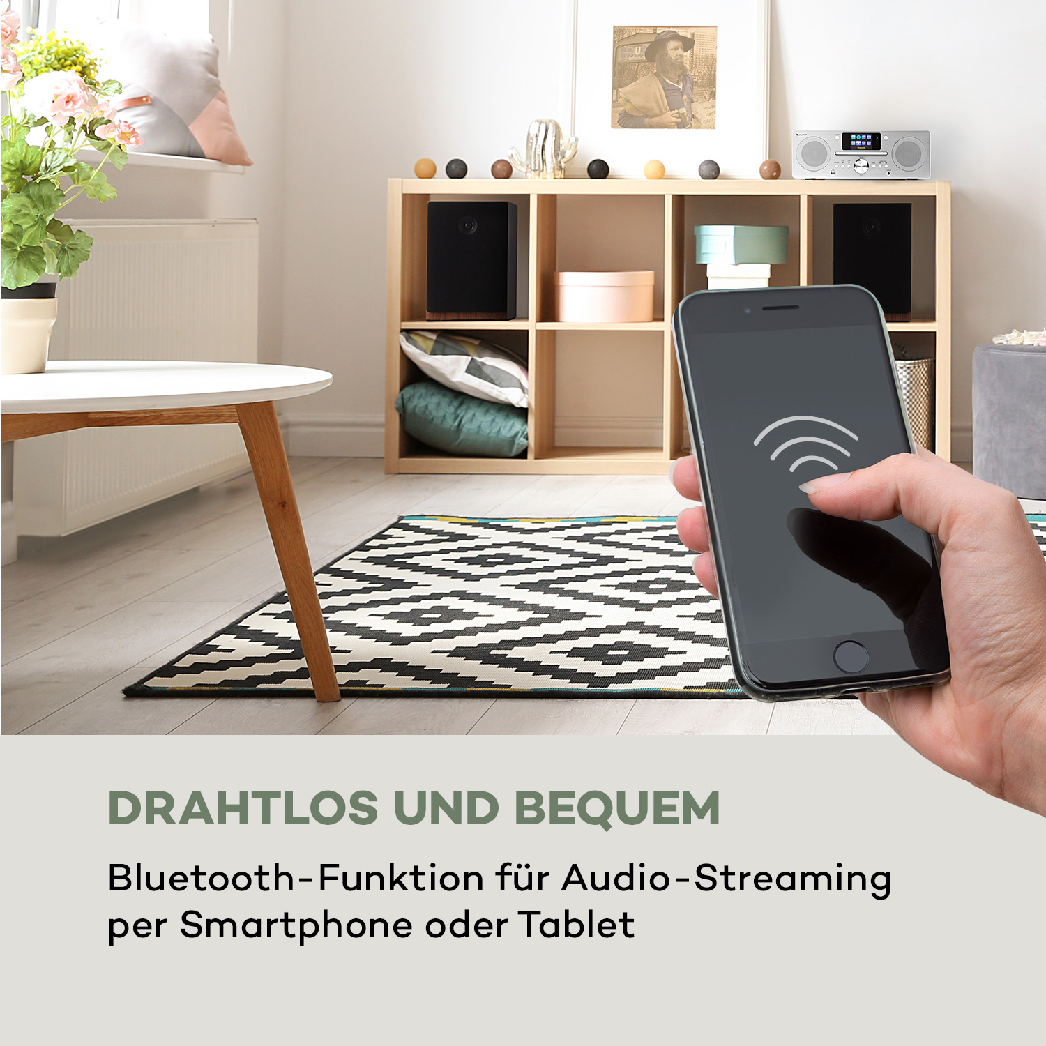Eine Person hält ein Telefon, im Hintergrund ein Wohnzimmer.