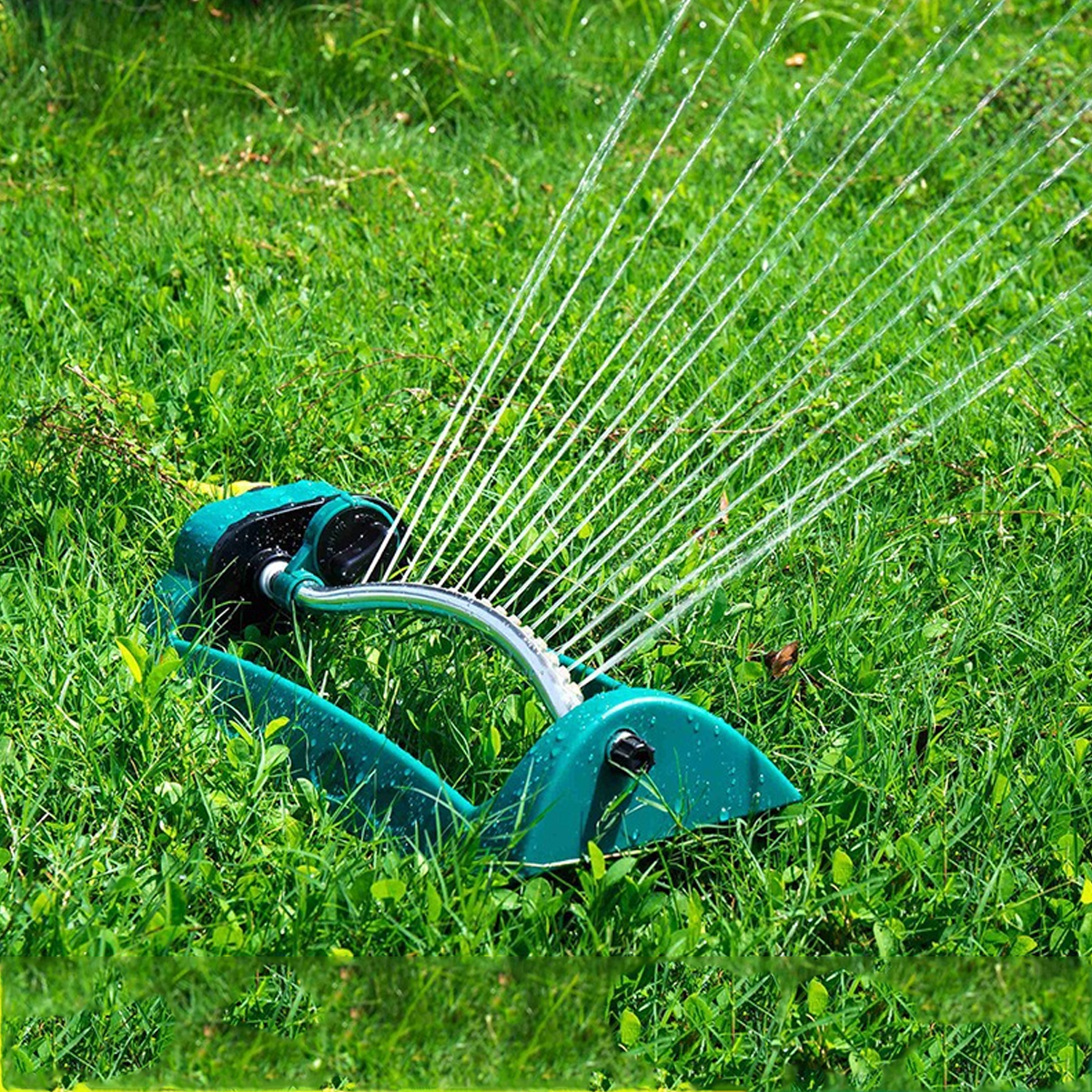 Un aspersor verde en hierba verde, rociando agua.