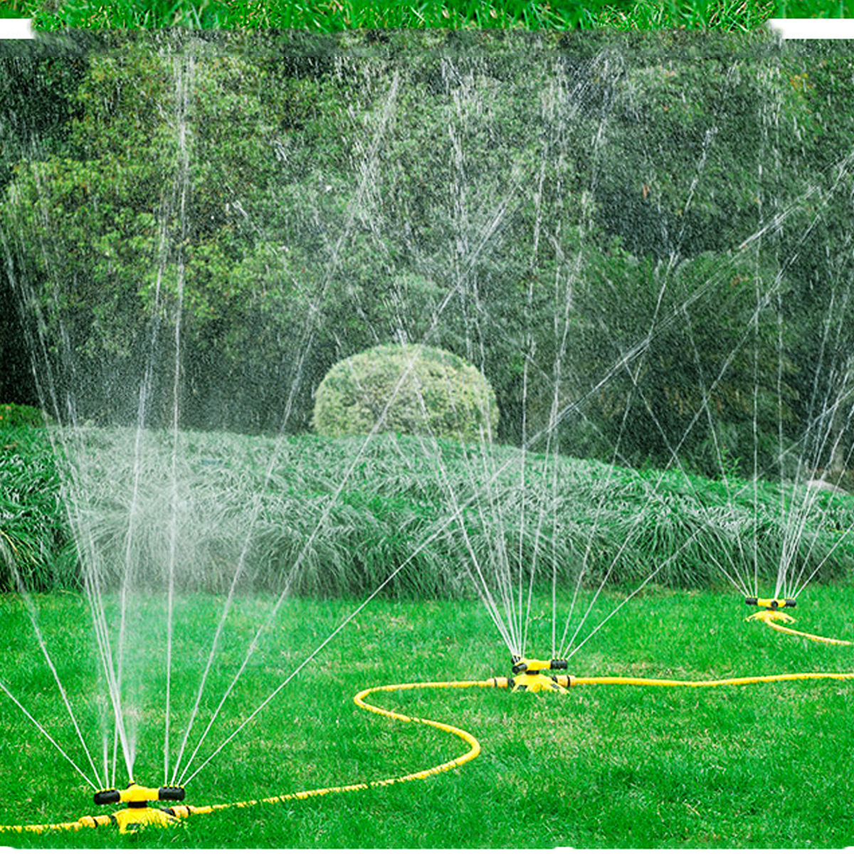 Aspersores de césped regando un césped verde. El agua sale de cada cabezal de aspersor, con árboles al fondo.