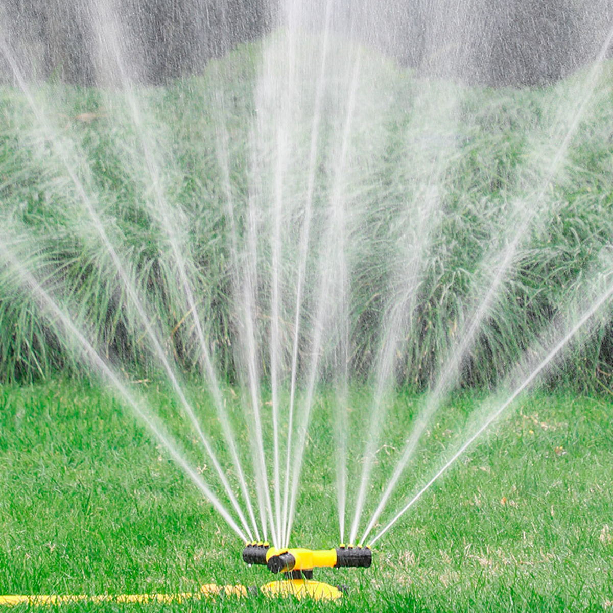 Aspersor rociando agua sobre césped. Fondo verde.