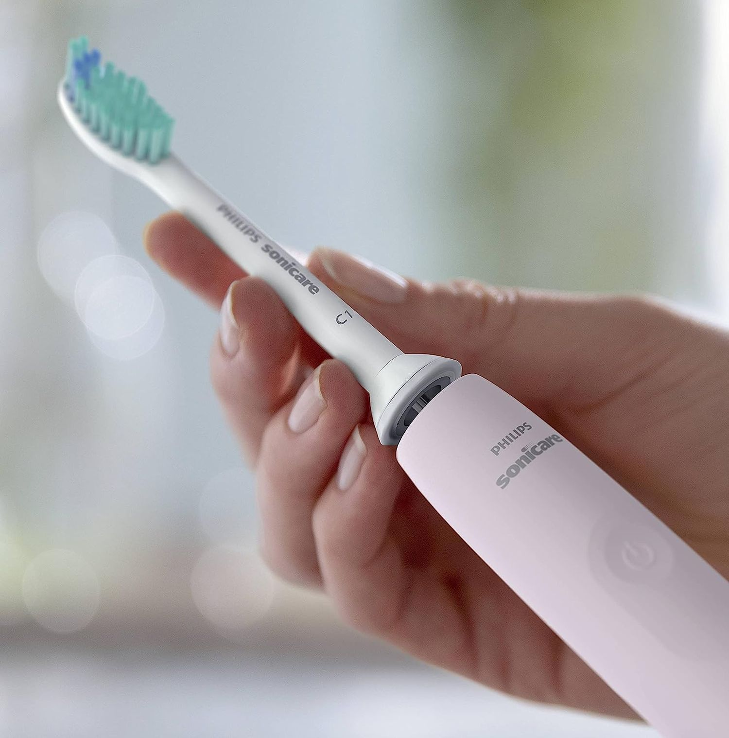 Ręka trzyma różową szczoteczkę do zębów Philips Sonicare z zielonym i niebieskim włosiem.