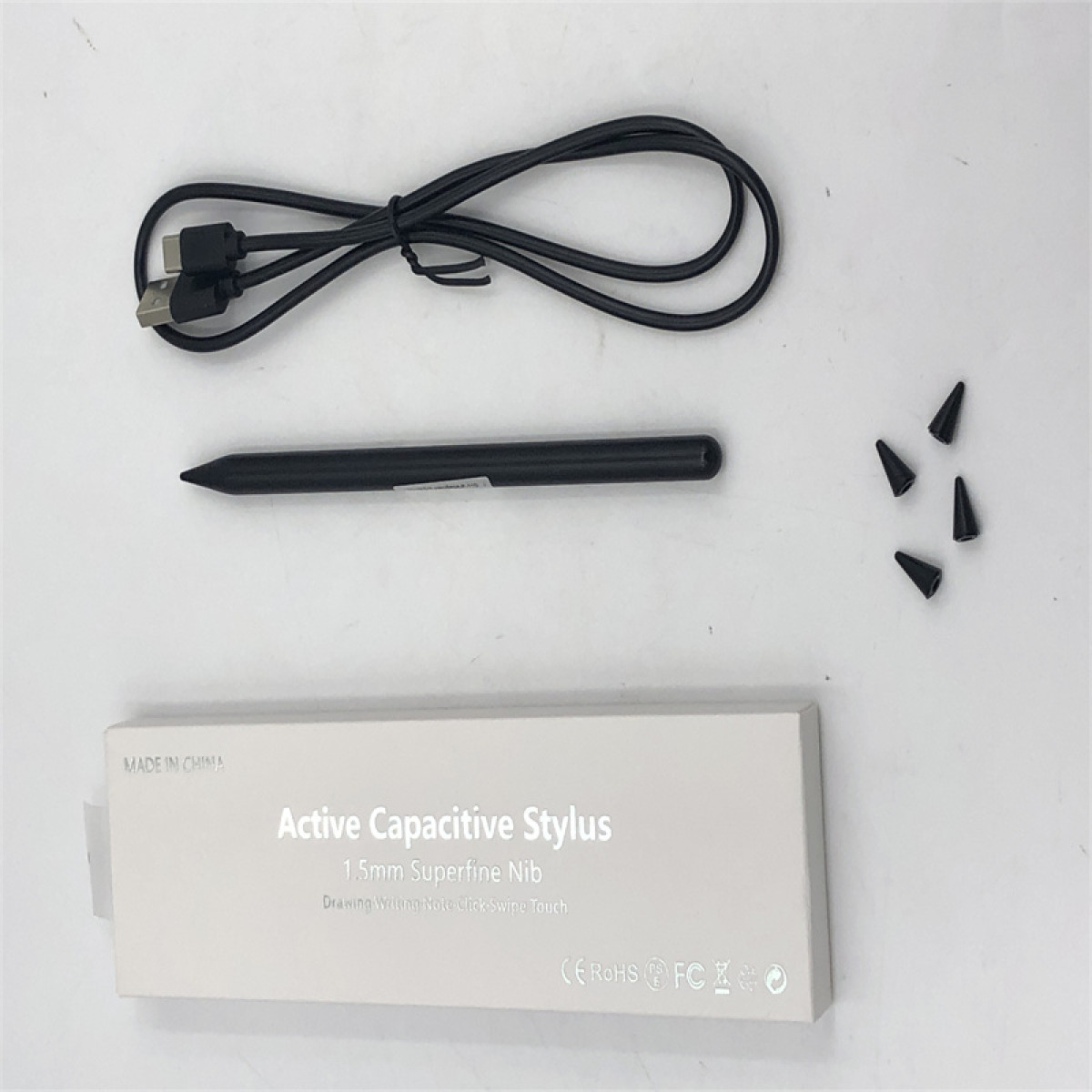 Weiße Box mit schwarzem Stift und zusätzlichen Spitzen. Schwarzes USB-Kabel. Weißer Hintergrund.