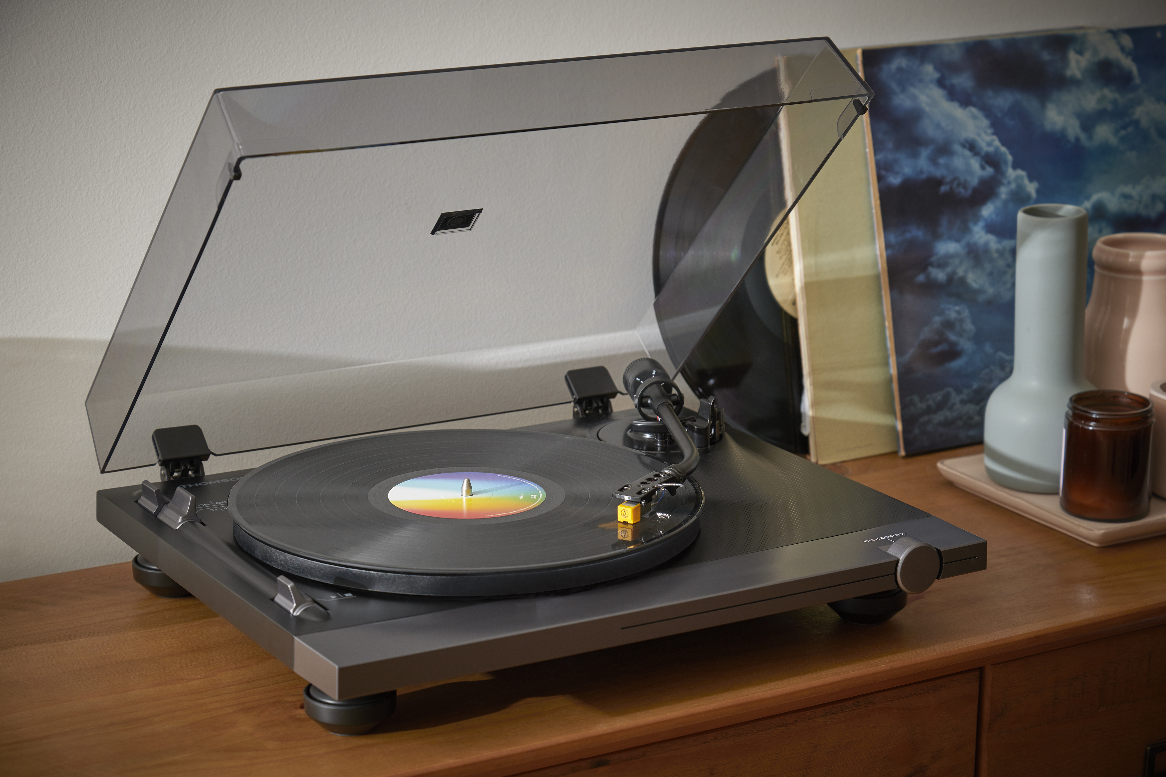 Gramofon z płytą. W tle kilka butelek, na drewnianym stole.