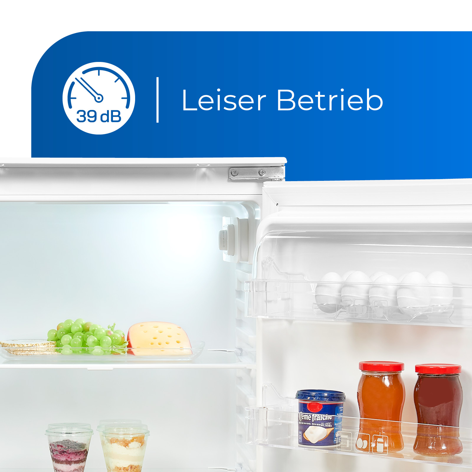 Interior de refrigerador abierto con estantes y alimentos. Etiqueta dice 'Leiser Betrieb'.