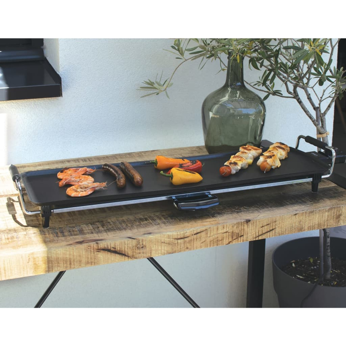 Grill mit gekochtem Essen auf einem Holztisch. Beinhaltet Garnelen, Würstchen und Paprika.