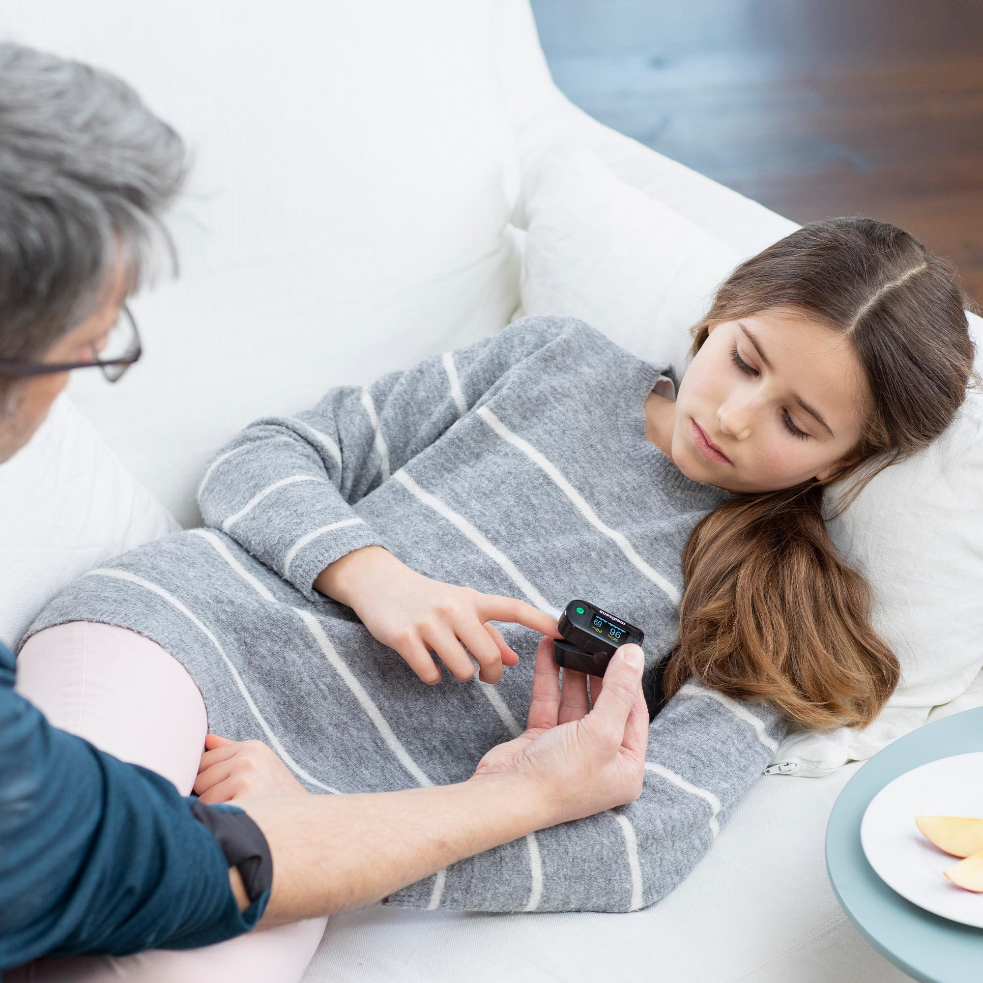 Mężczyzna testuje palec dziewczyny za pomocą urządzenia medycznego na kanapie.
