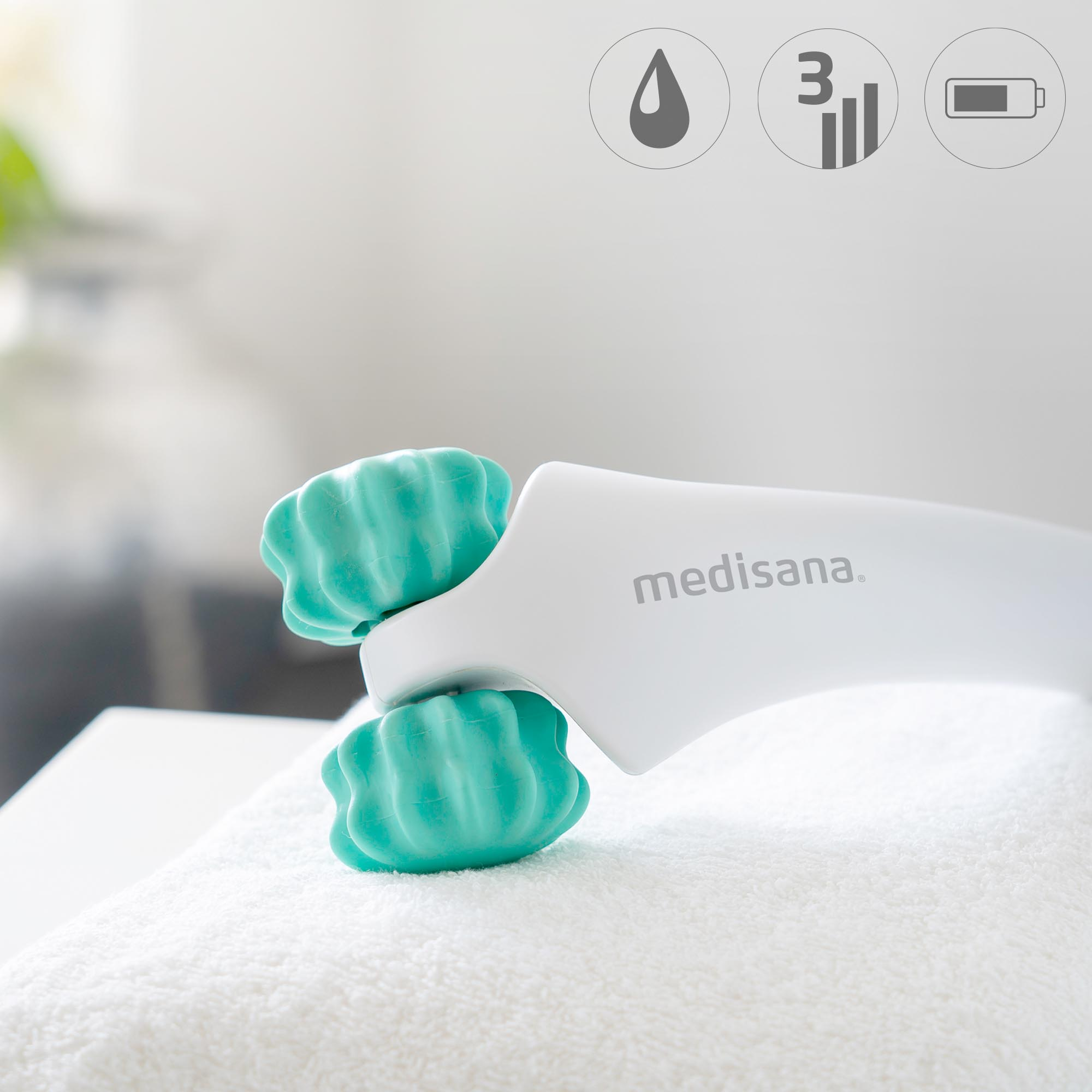 Hand-Gesichtsmassagegerät mit zwei teal Rollen. Weißer Griff auf Handtuch.