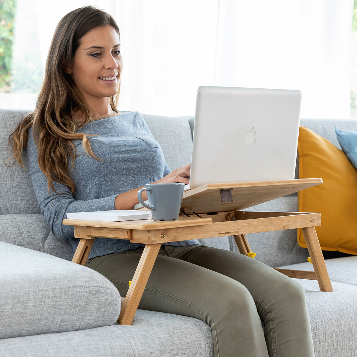 Una donna seduta su un divano che usa un laptop su un tavolo per laptop in bambù.