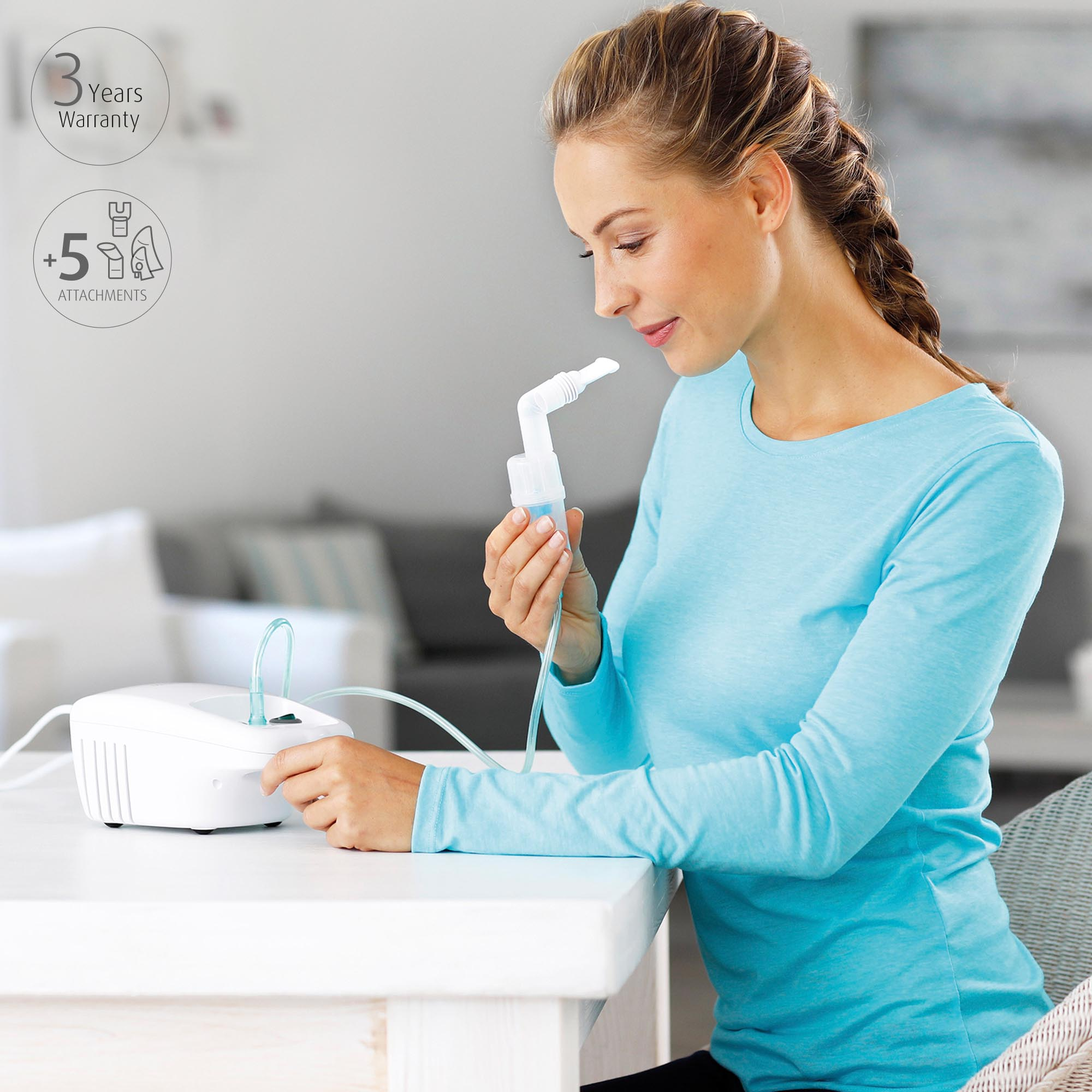 A woman holding a nebulizer, sitting at a white table with attachments and warranty info.