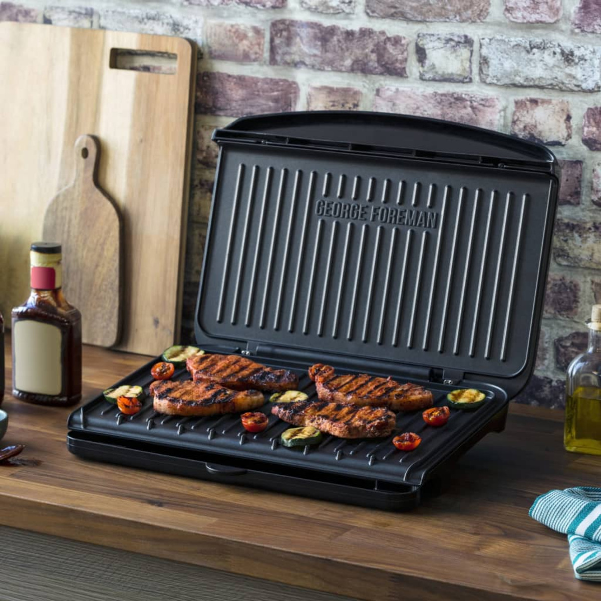 George Foreman Grill mit gegrilltem Fleisch, Tomaten und Zucchini auf einem Holztisch.