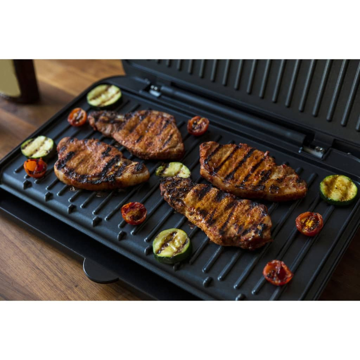 Grill mit gegrillten Schweinekoteletts und Gemüse. Der Grill ist schwarz, und das Essen ist schön angerichtet.