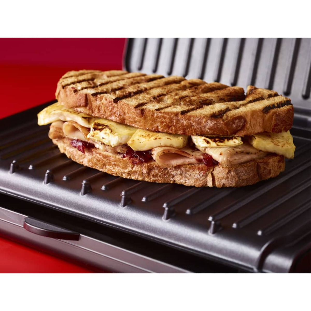 Ein gegrilltes Sandwich auf einem schwarzen Grill, Zutaten sichtbar.
