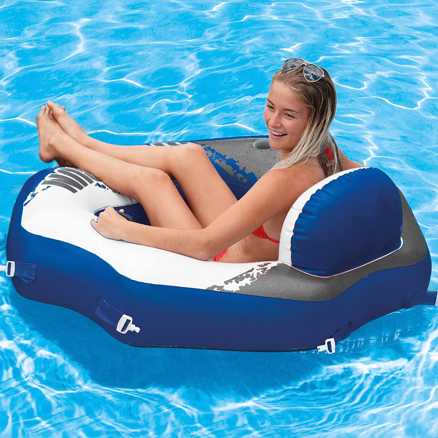Frau im Pool auf blau-weißem Schlauchboot, roter Bikini, Sonnenbrille.