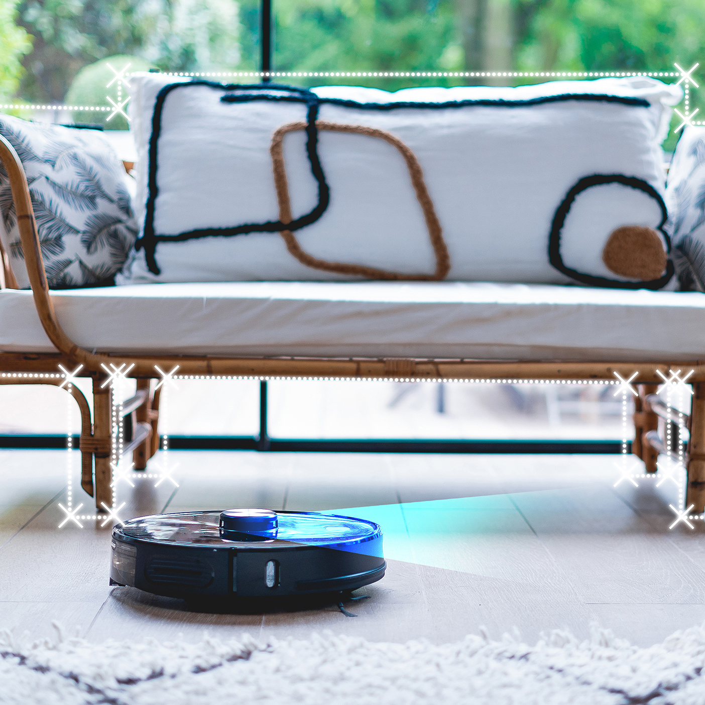 Schwarzer Roboter-Staubsauger auf Holzboden. Im Hintergrund ein weißes Sofa mit Kissen.