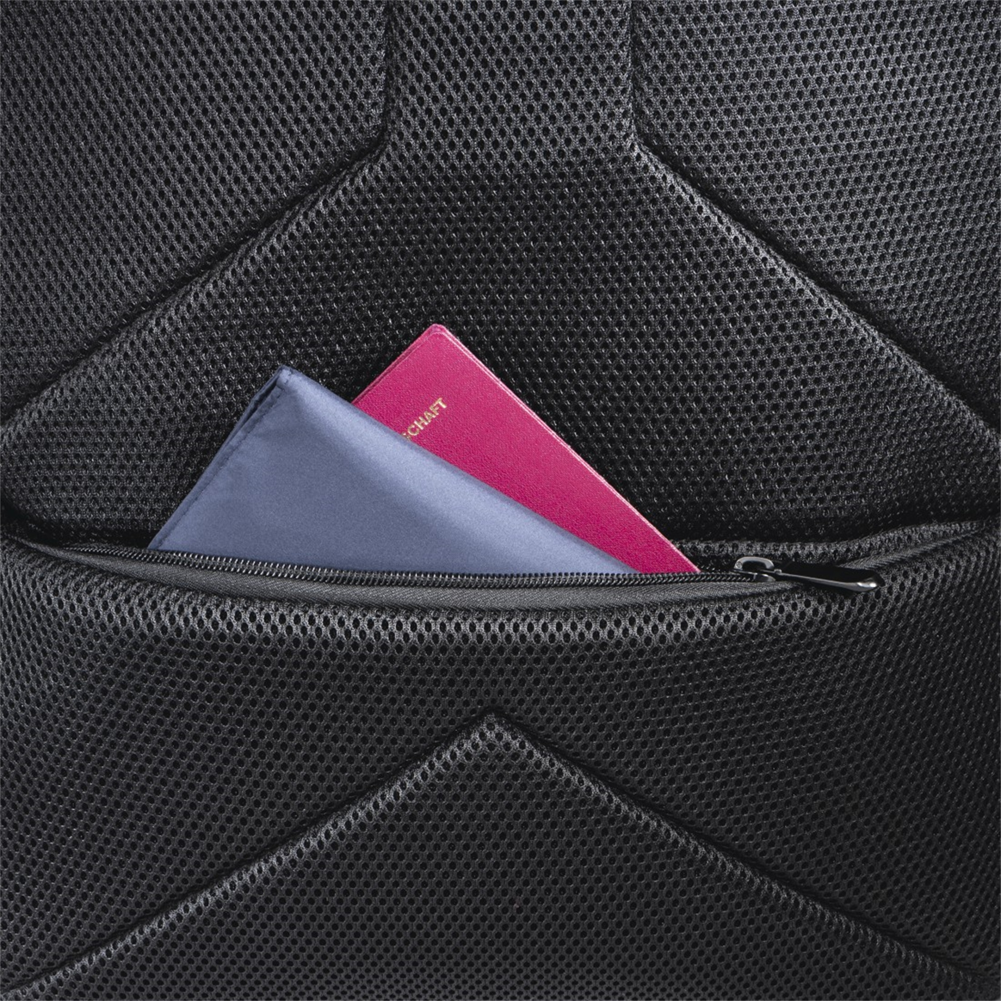 Nahaufnahme einer schwarzen Rucksacktasche mit einem gefalteten blauen Tuch und einem rosa Reisepass.