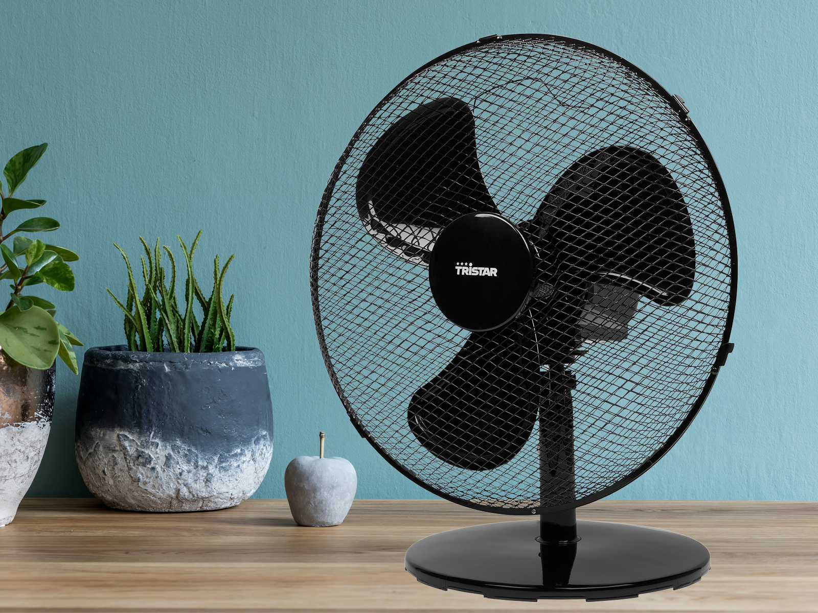 Ein schwarzer Tischventilator mit Schutzgitter auf einem Holztisch.
