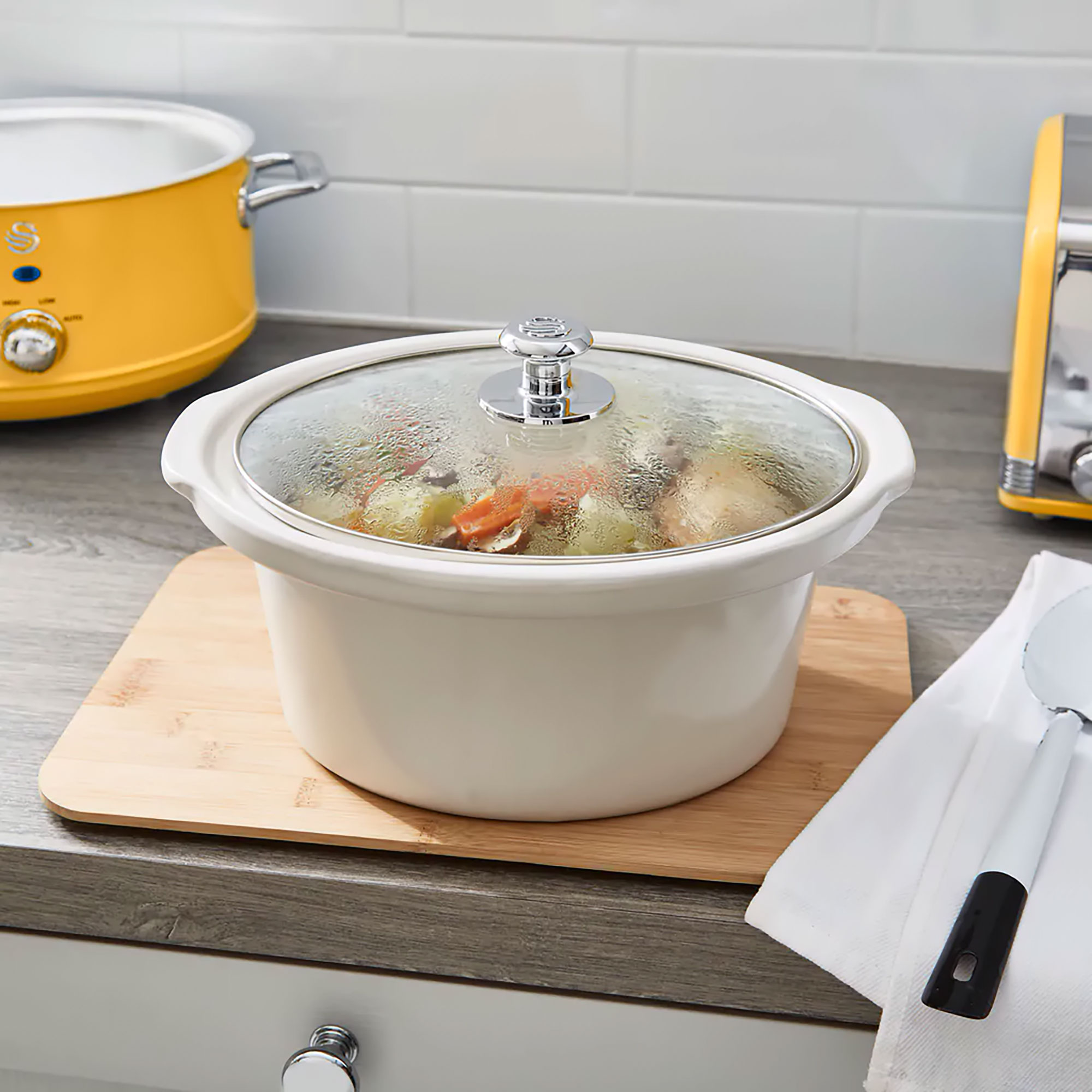 Crockpot mit Essen darin auf einem Holzbrett mit einem weißen Handtuch auf einer Theke.