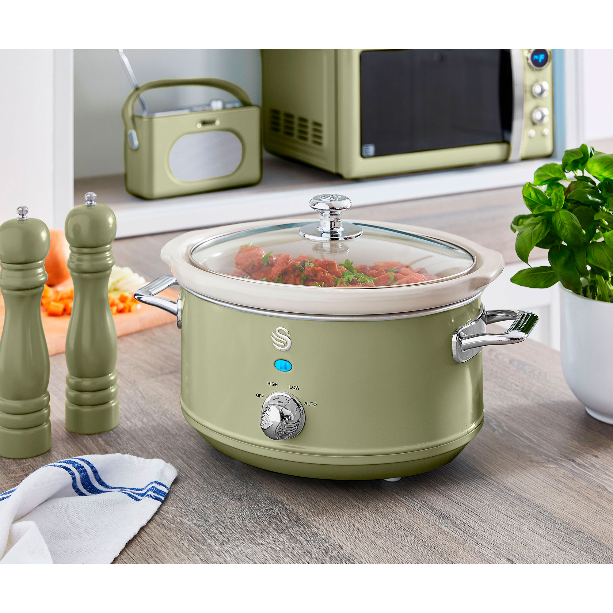 Ein Slow Cooker mit Essen, neben Salz- und Pfefferstreuern und einem kleinen Radio. Alles auf einem Holztisch.