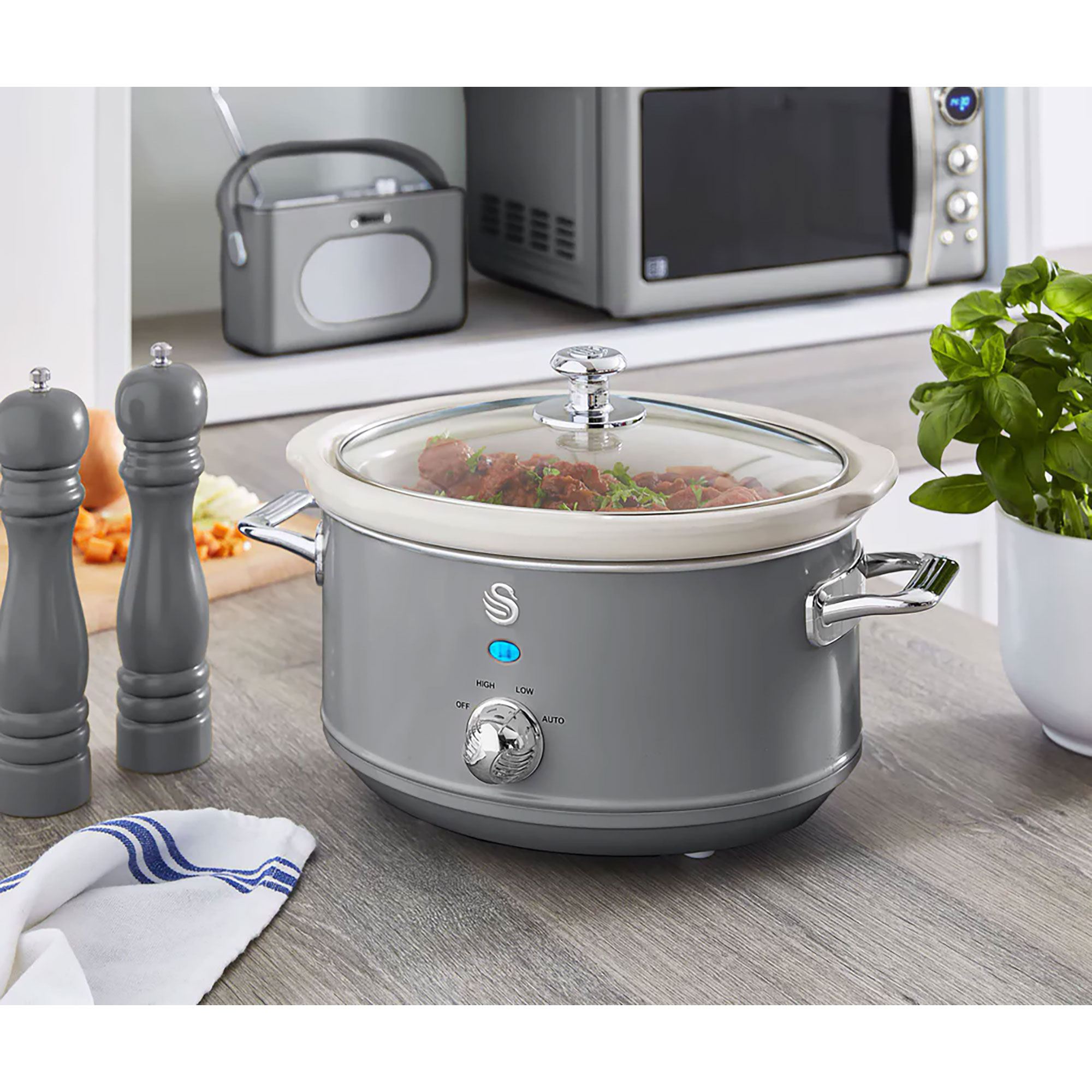 Ein grauer Slow Cooker mit Glasdeckel, Essen sichtbar, mit Salz- und Pfefferstreuern.