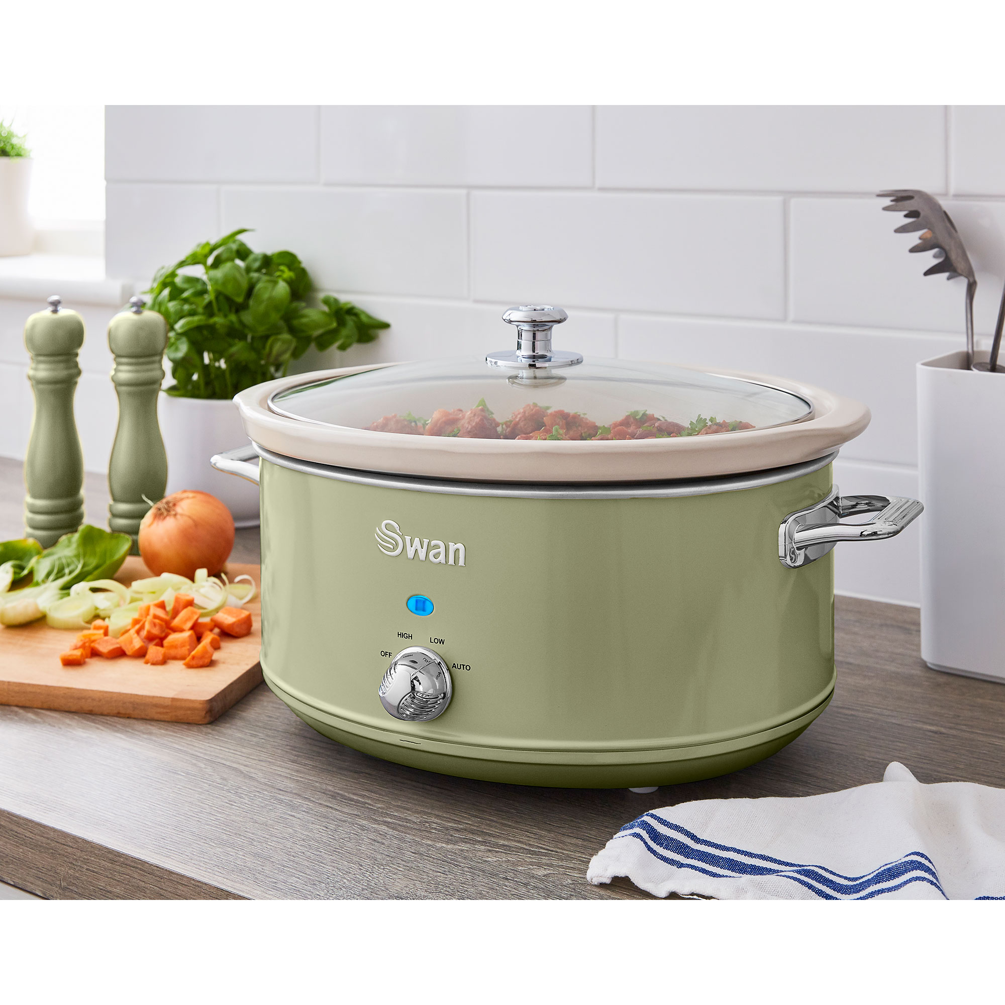 Una olla de cocción lenta verde sobre una superficie de madera, con verduras e ingredientes cerca, y un fondo blanco.