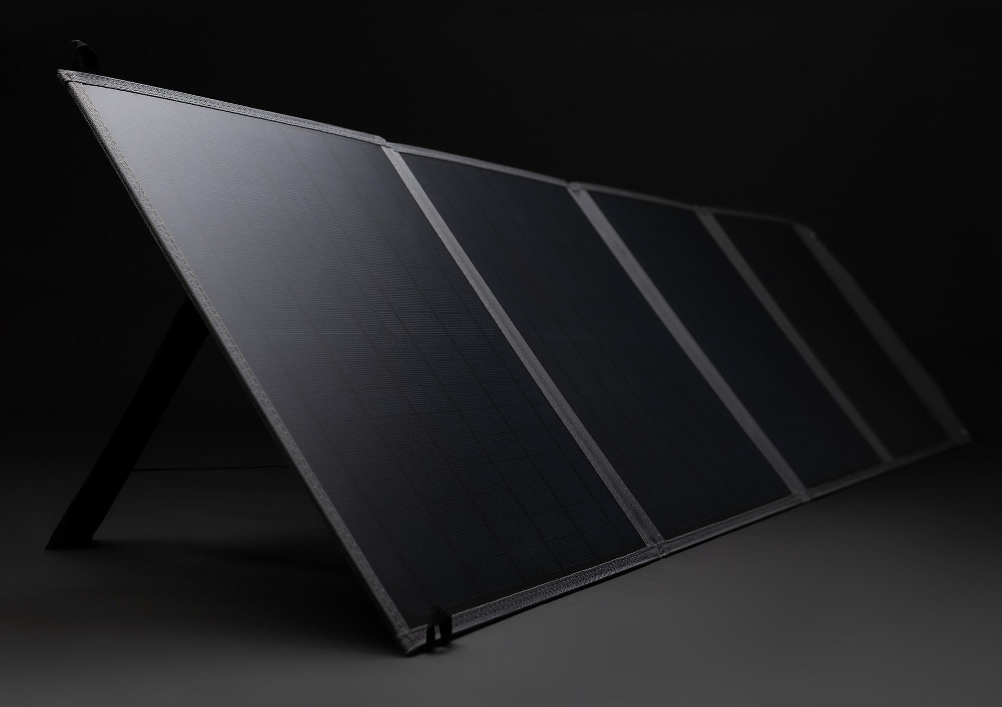 Faltbares Solarpanel, schwarz mit grauem Rand, vor dunklem Hintergrund.