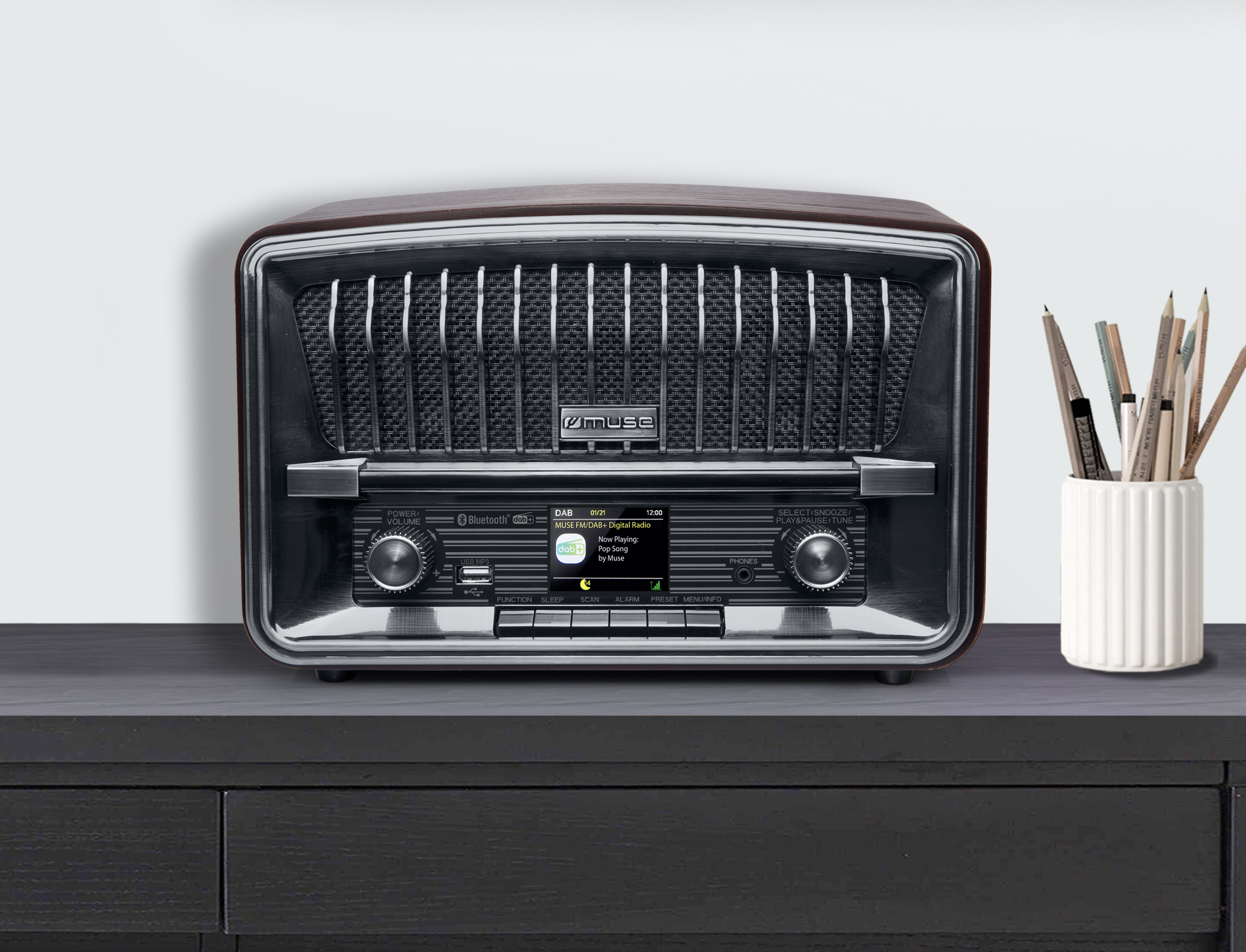 Radio de estilo vintage sobre una superficie oscura, con una pantalla digital y un portalápices a la derecha.