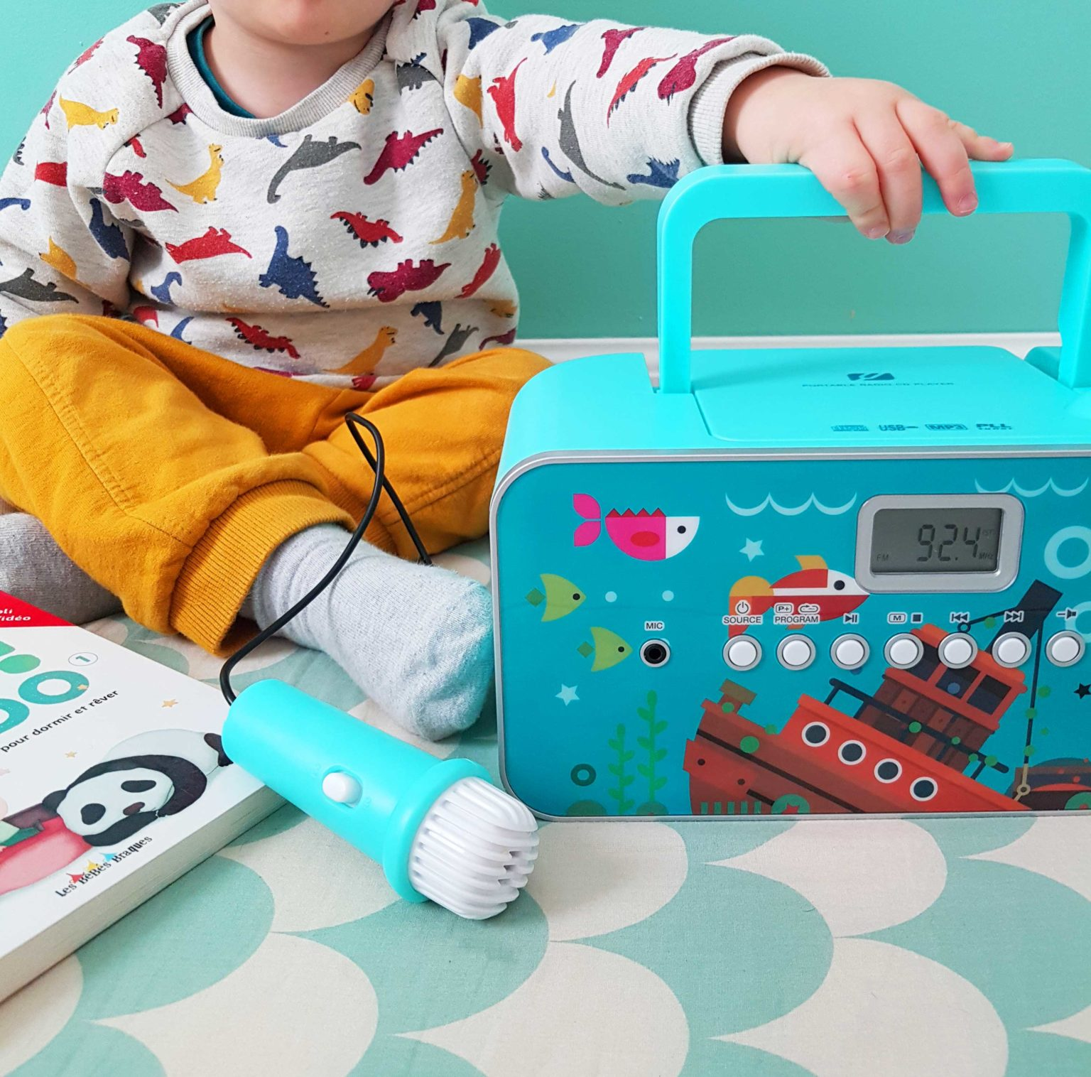Un enfant avec une radio et un microphone jouet. La radio est bleue et décorée de poissons et d'un bateau.