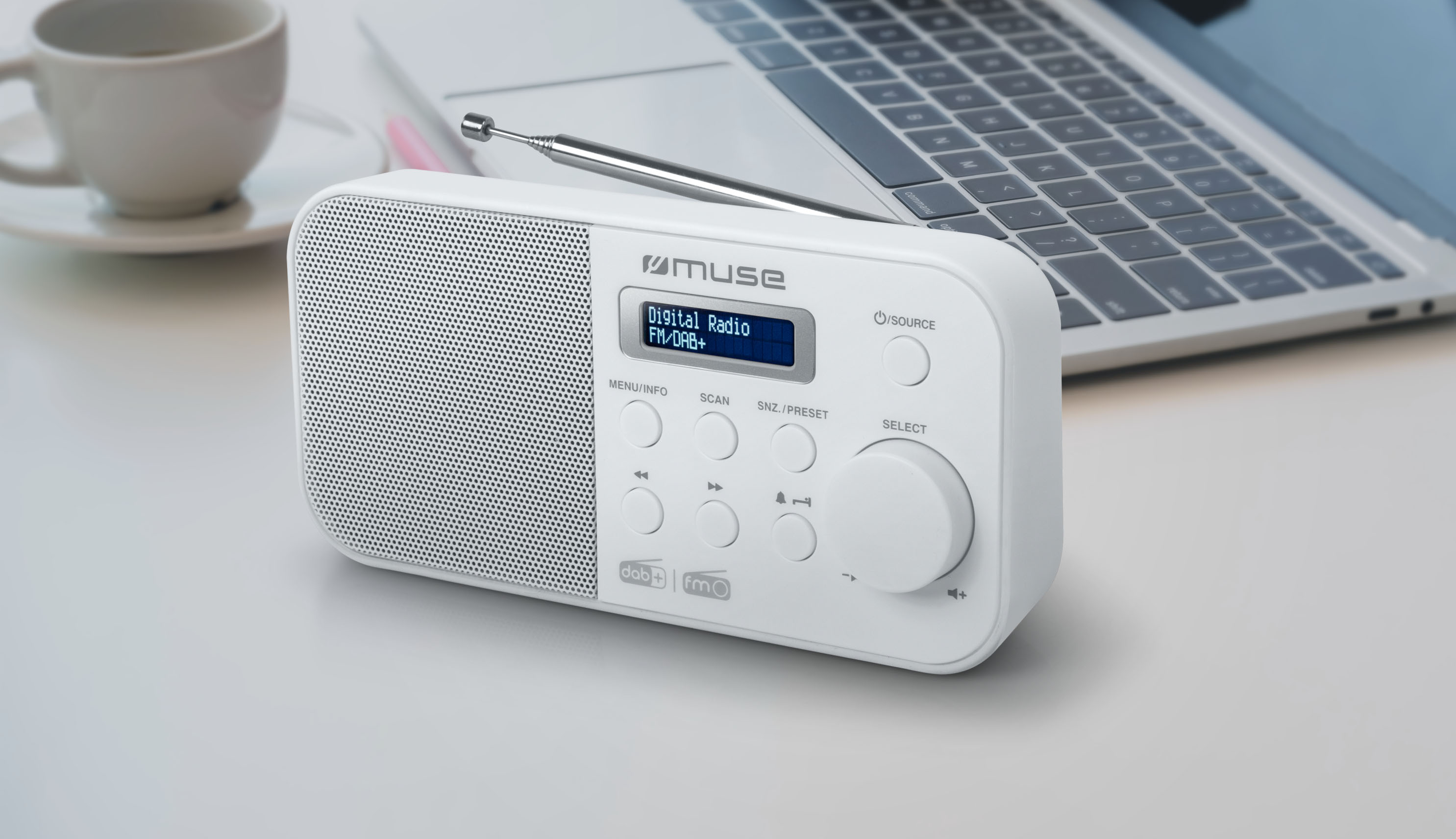 Białe radio z anteną na biurku, obok laptopa i filiżanki.