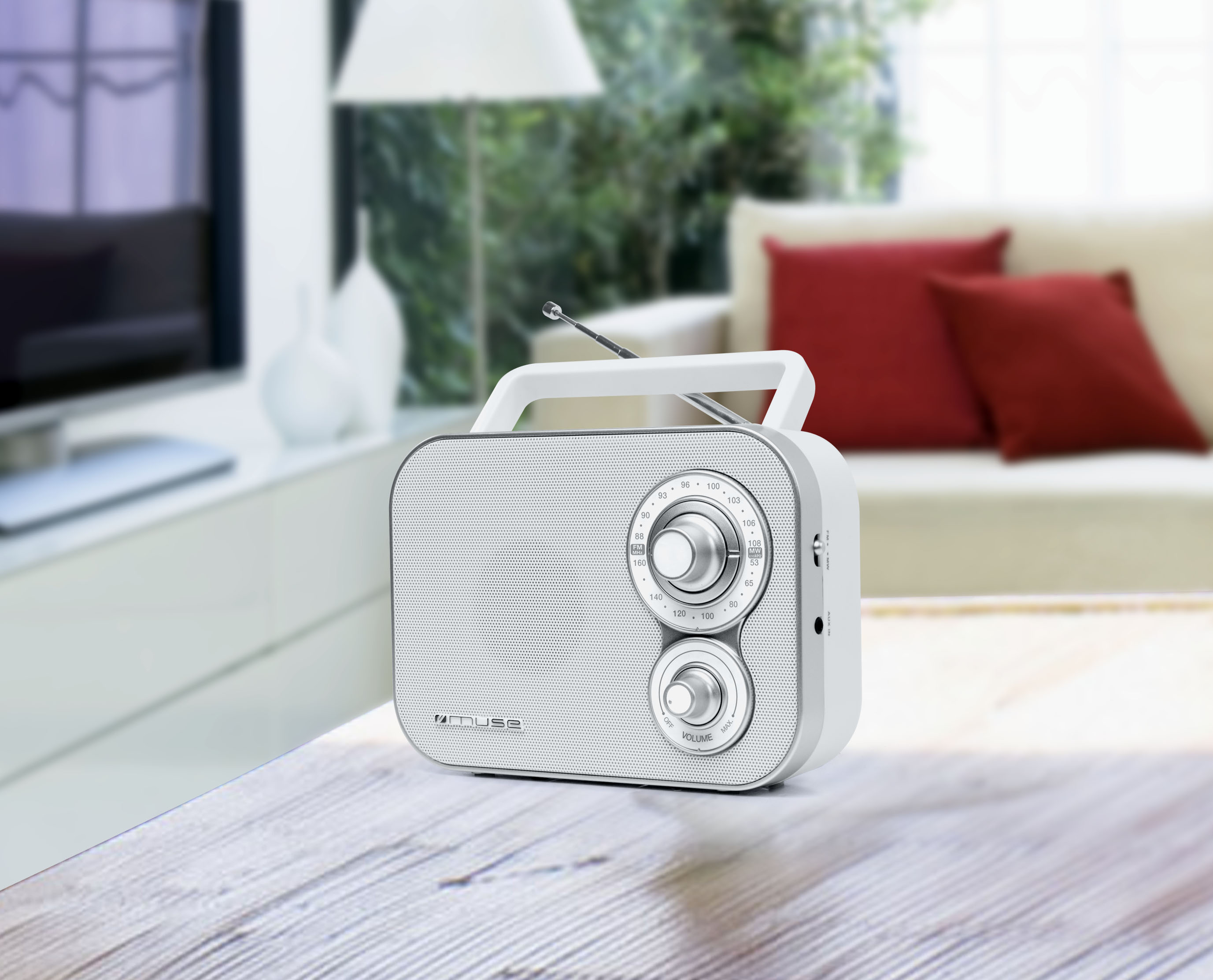 Białe radio przenośne na drewnianym stole. W tle rozmyty salon.